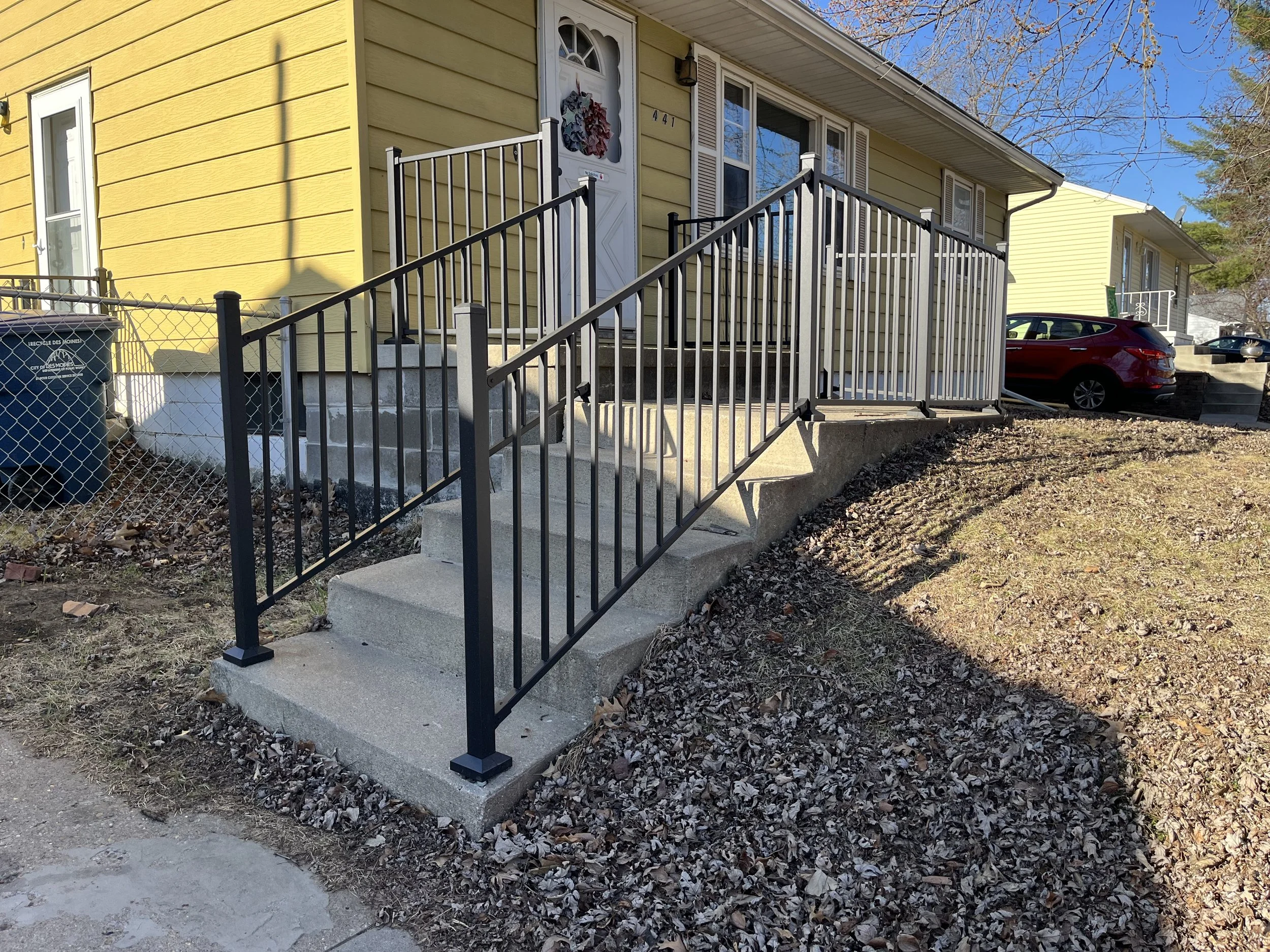Black aluminum handrail installed in Des Moines, IA around a front porch and down the entry stairs for added strength, stability, and safety. This sturdy, low-maintenance railing provides a clean, modern look and was professionally installed by Post 
