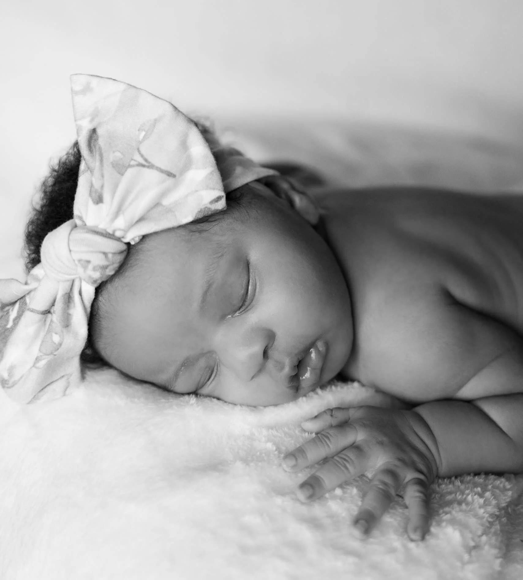 Close-up of a sleeping baby wearing a floral headband, resting on a soft blanket.