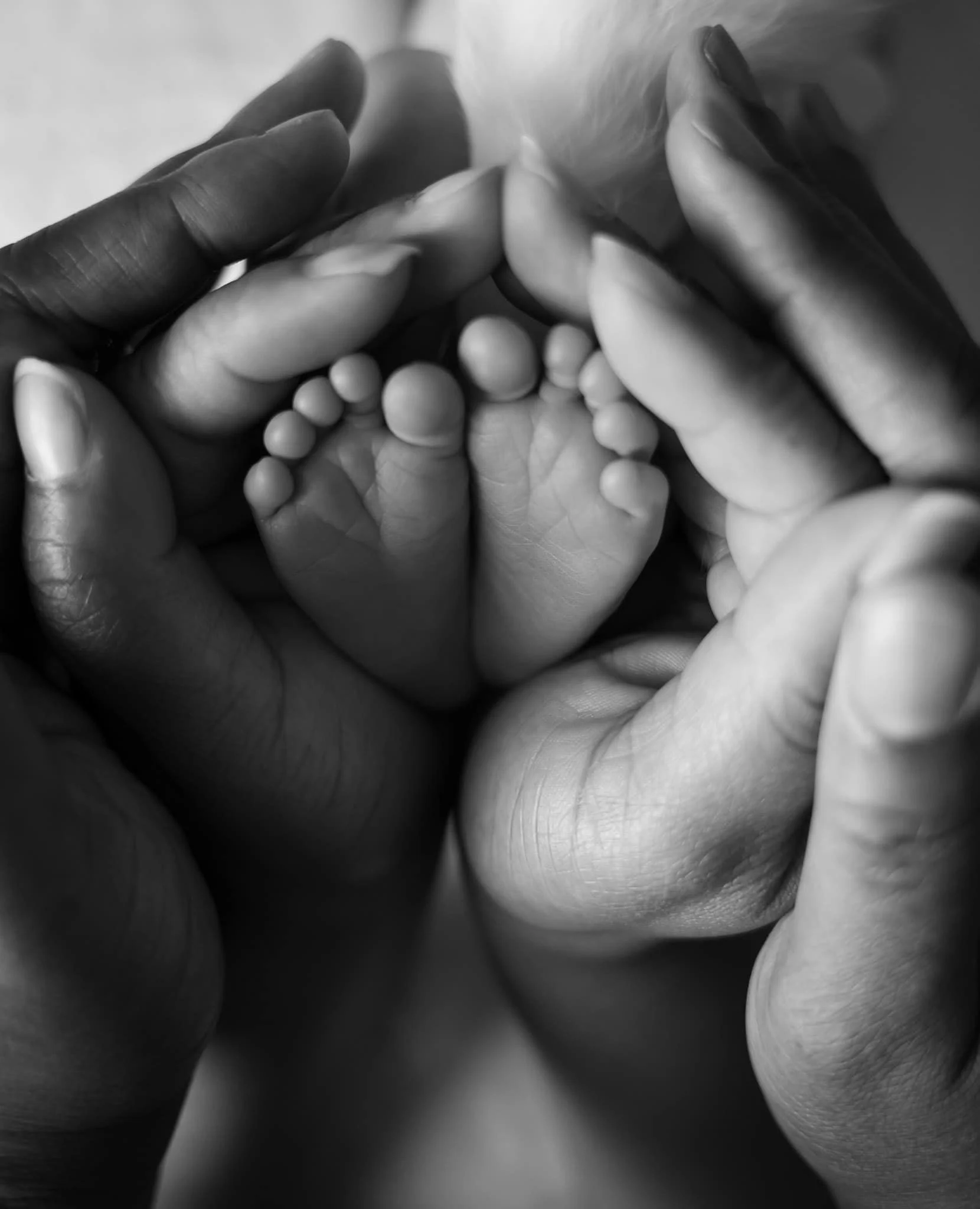 Close-up black and white photo of multiple hands gently holding a small object, likely beads or small balls, with a soft focus and intimate composition.