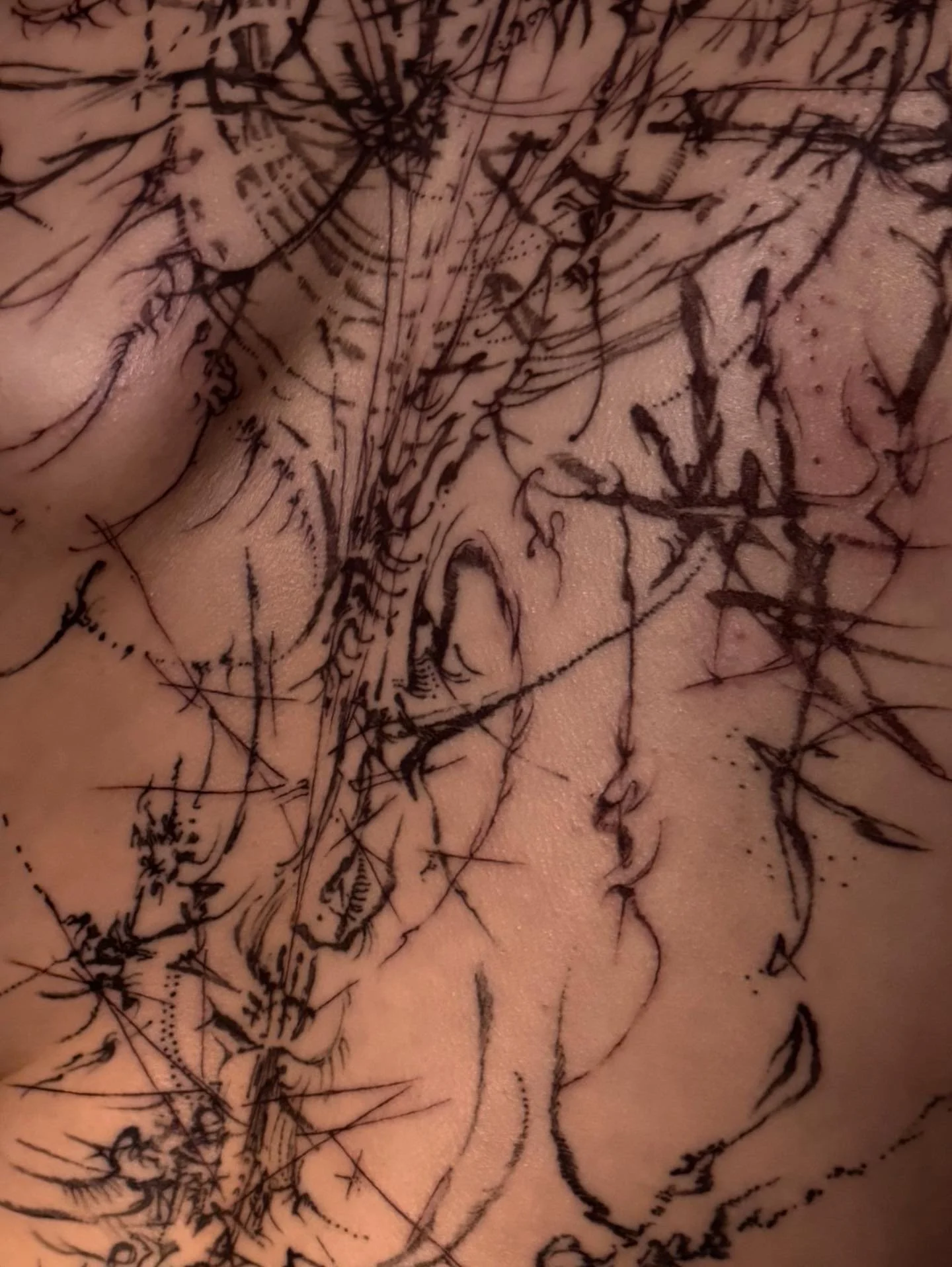 Close-up of a person's skin with a detailed, black line tattoo that has abstract and curly lines.
