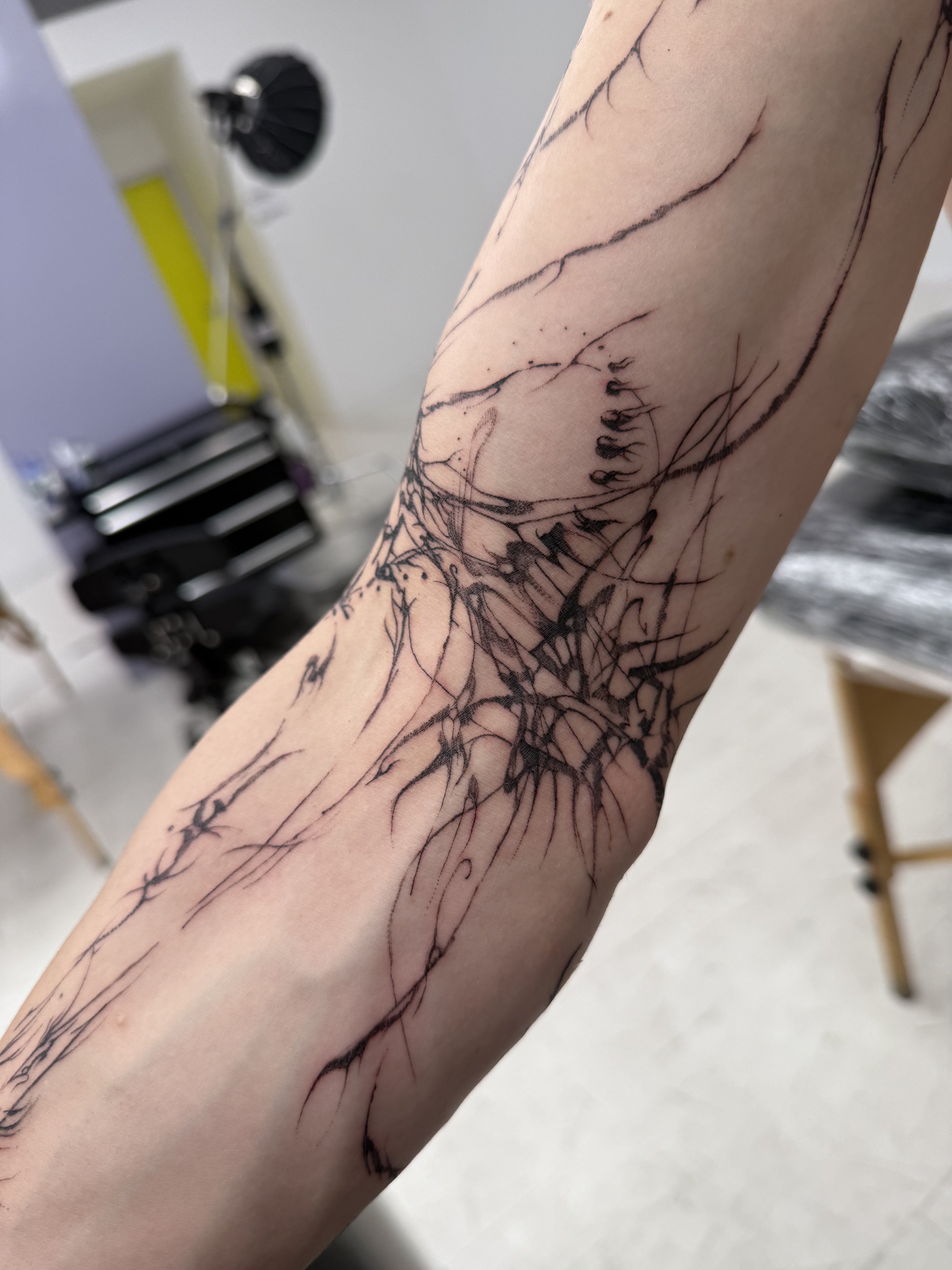 A person's forearm with a tattoo design of abstract black lines and cracks, resembling a web or shattered glass pattern.