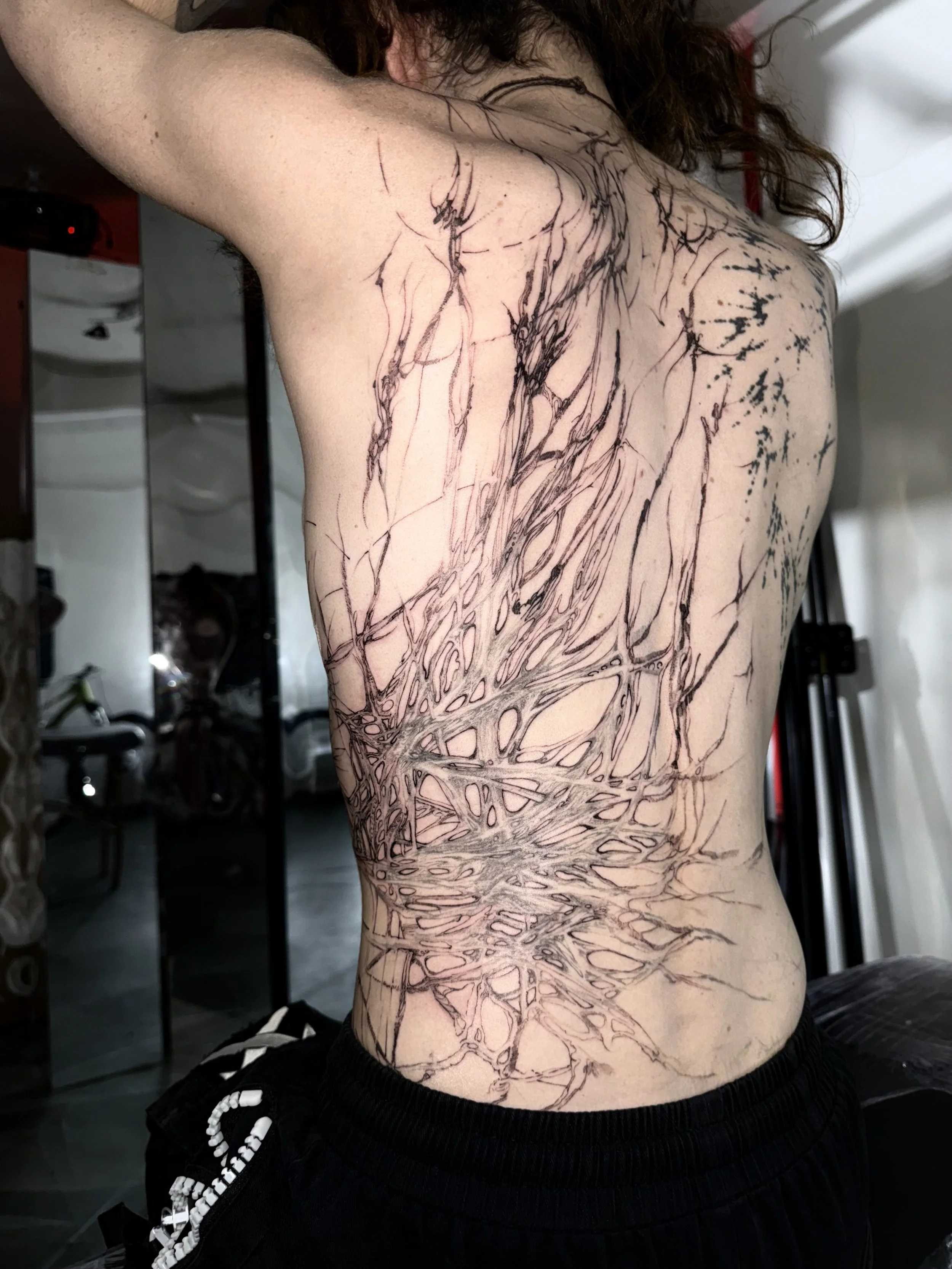A person with partially completed black ink tattoo of tree roots and branches on their side and back.