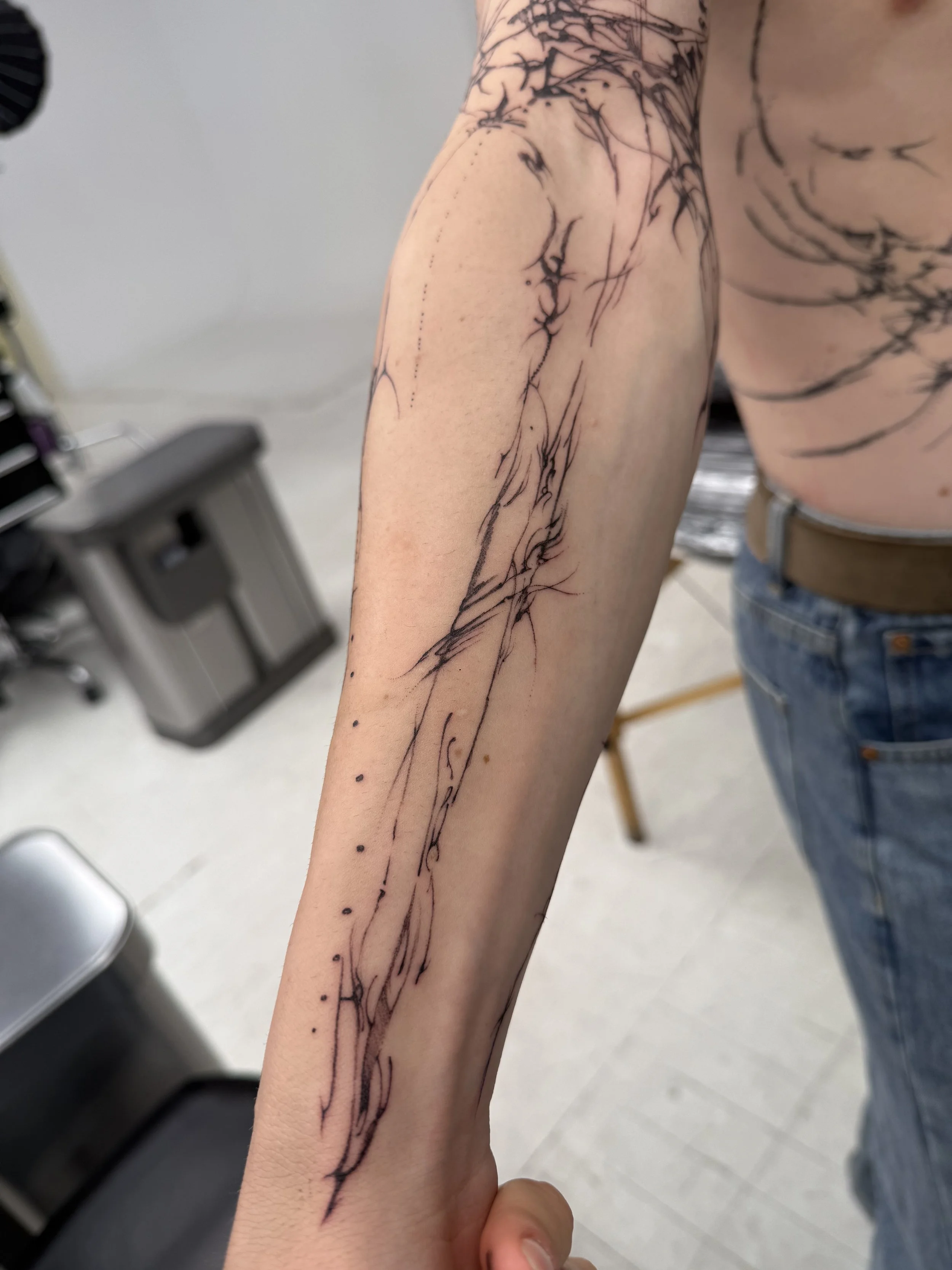 Tattoo artist holding a person's arm showing a fresh abstract line tattoo with black ink and fine lines.