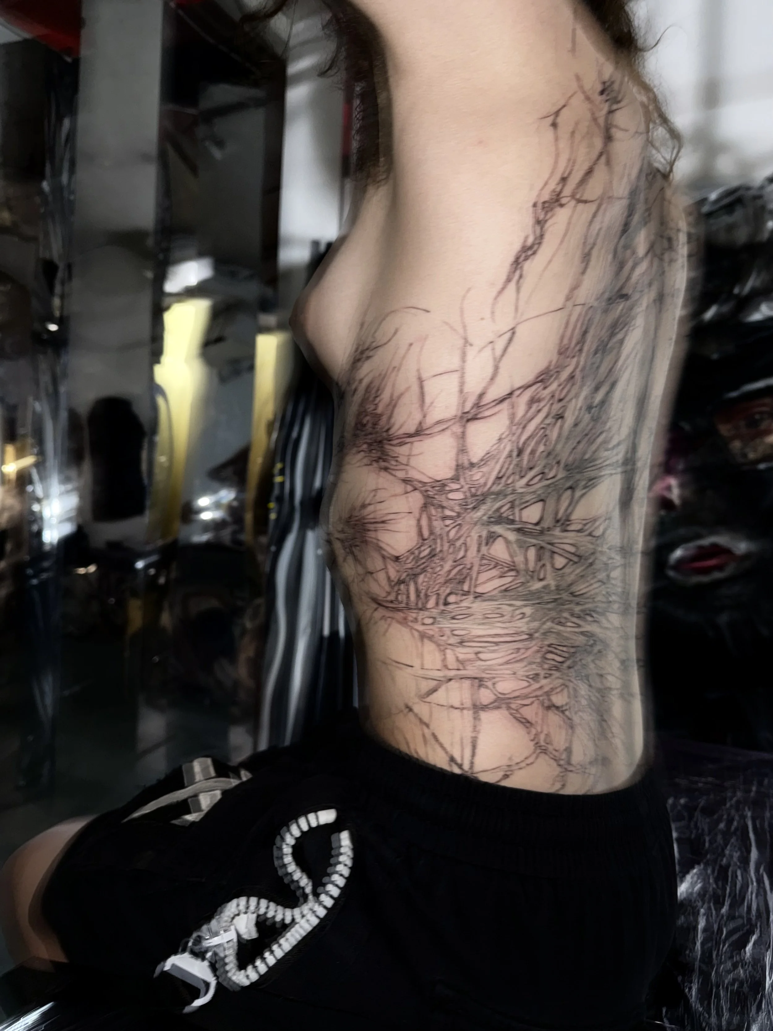 Side view of a person's torso with a tattoo outline of a tree with branches covering the stomach and ribcage.