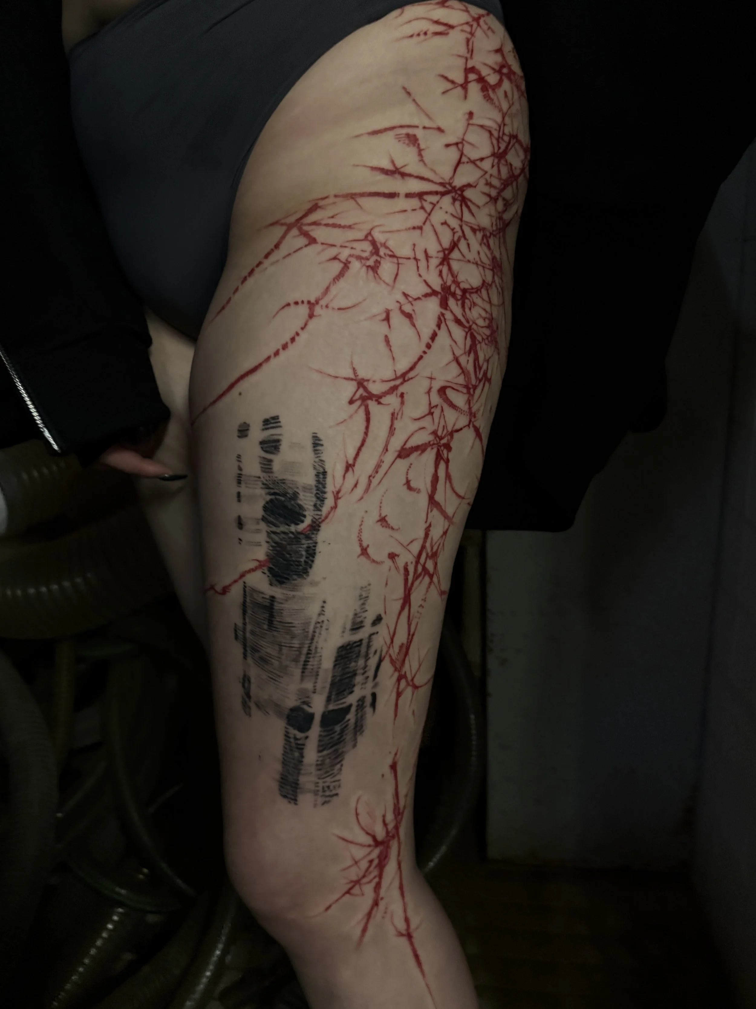 A person's thigh with red vein-like tattoos and a large barcode tattoo.