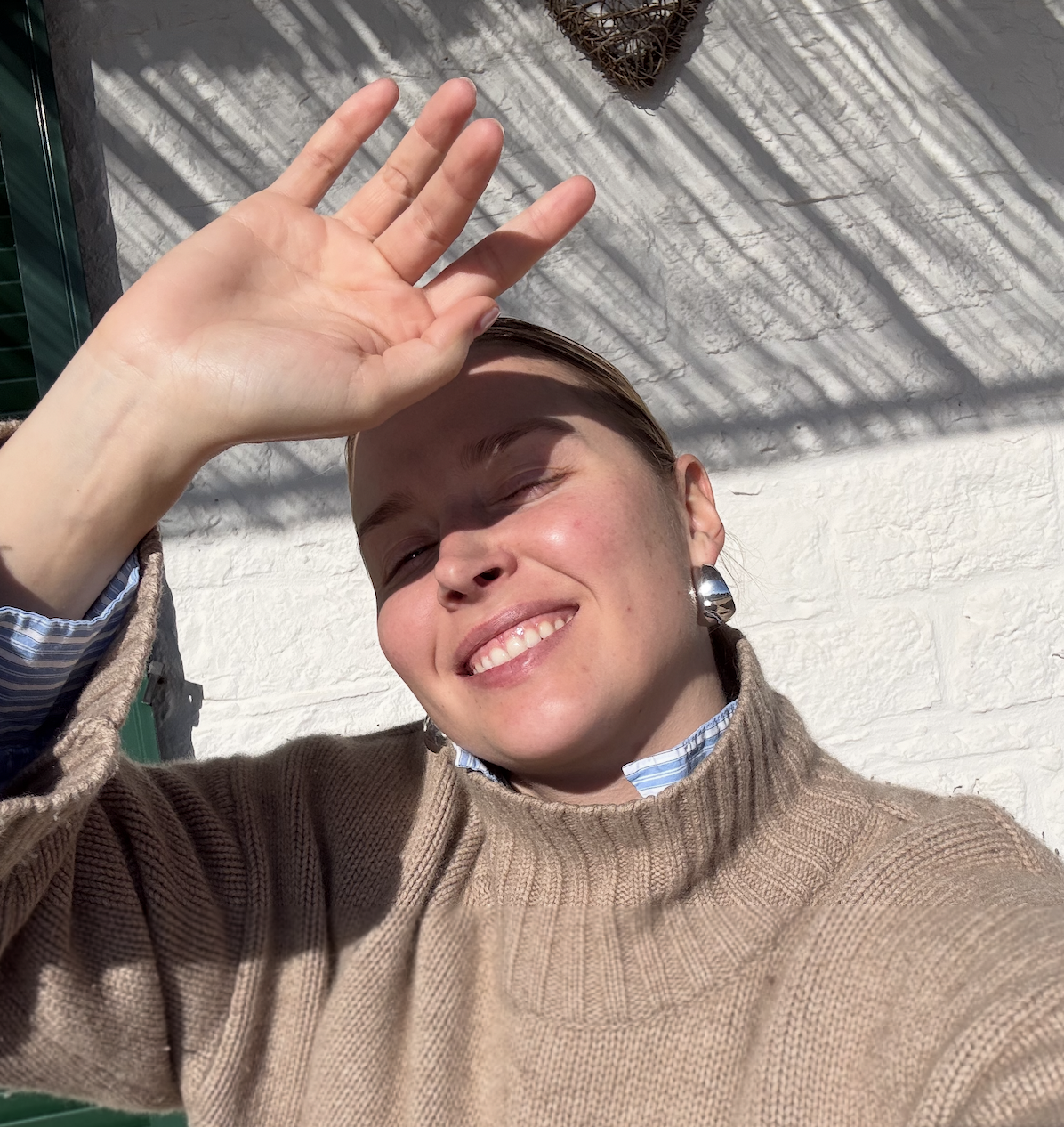 frau die in die kamera schaut und lächelt in der sonne mit hand vom gesicht um sich vor der sonne zu schützen