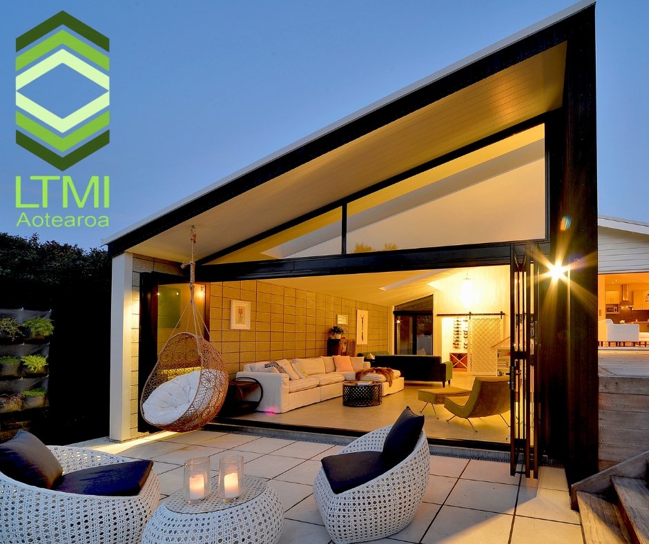 Modern house with large glass doors open to outdoor patio, interior living room with beige sectional, hanging egg chair, and outdoor seating with candles.