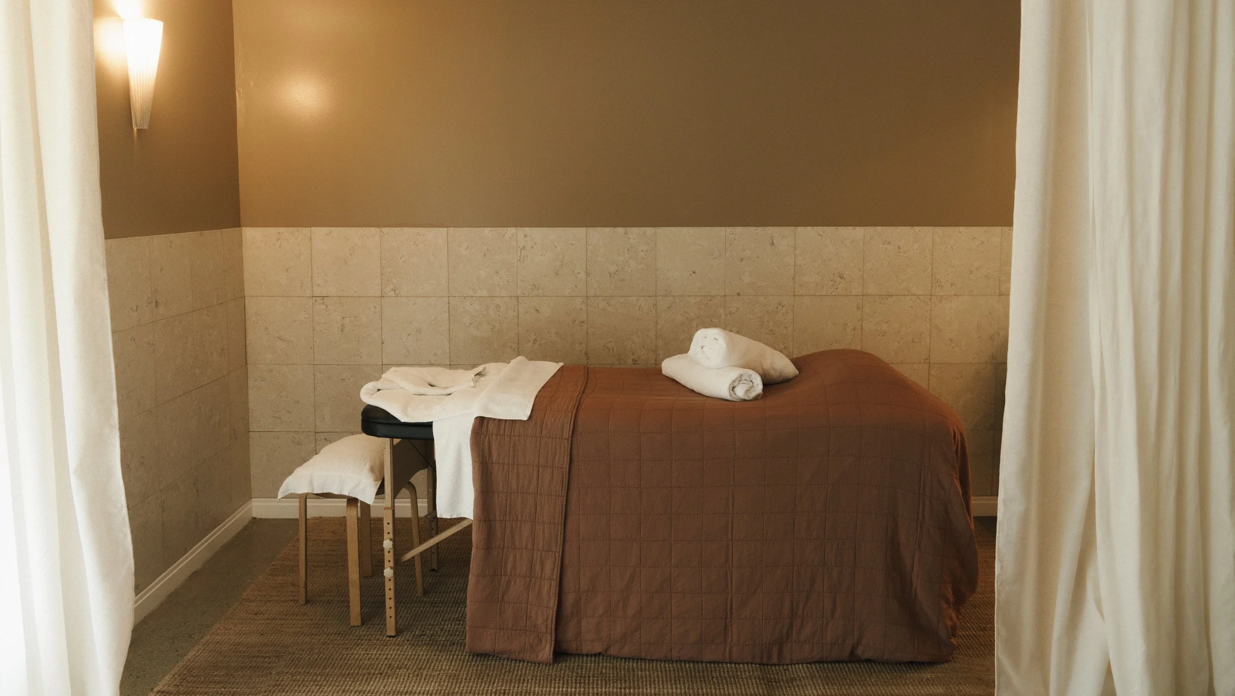 Massage table with red clay linens and two rolled white towels, representing a healer’s workspace supported by a virtual assistant for digital launches, content marketing, SEO, and admin.