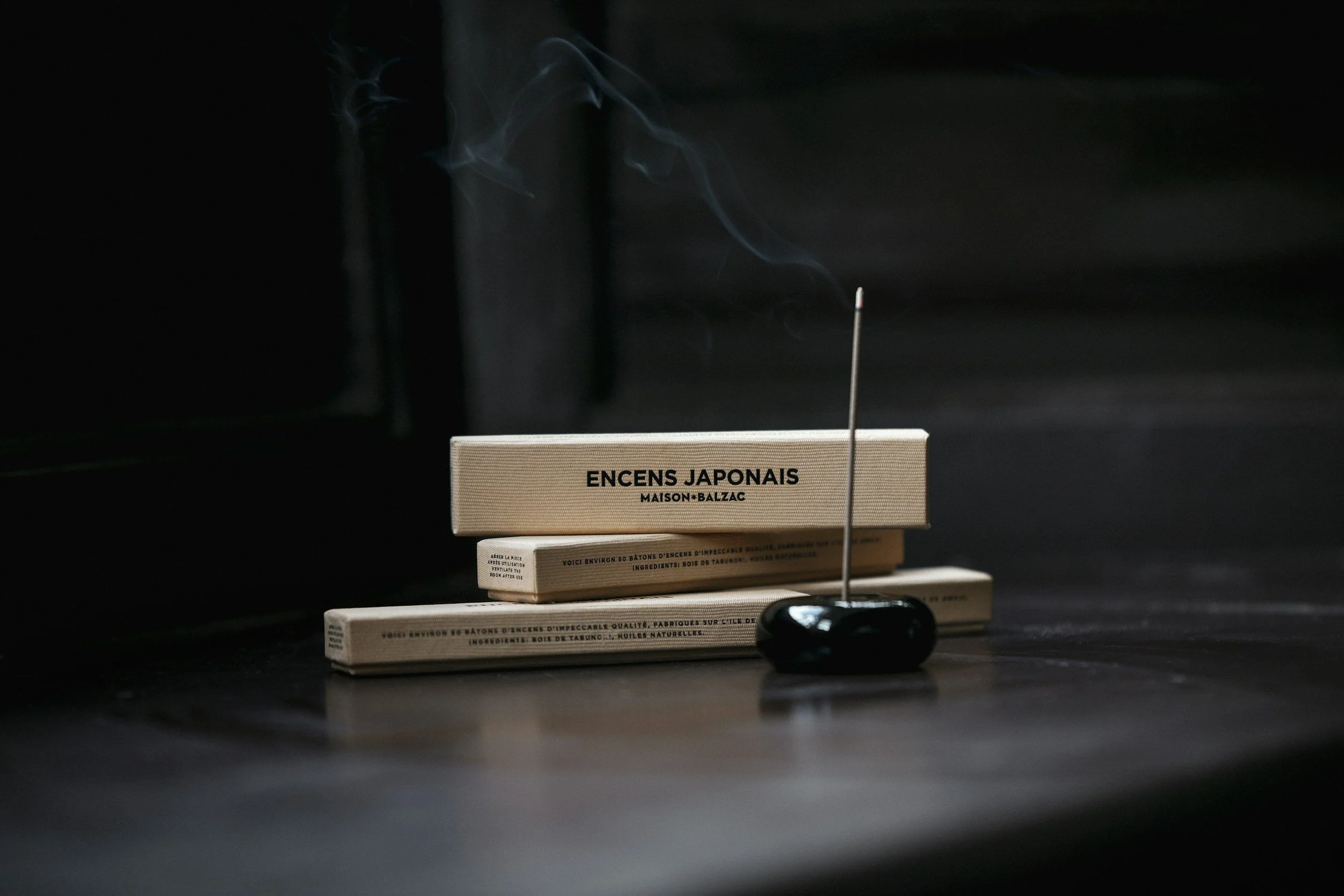 Black tabletop with three white incense boxes and a black incense holder with burning stick, representing a healer’s wellness space supported by a virtual assistant for digital launches, content marketing, SEO, and admin.