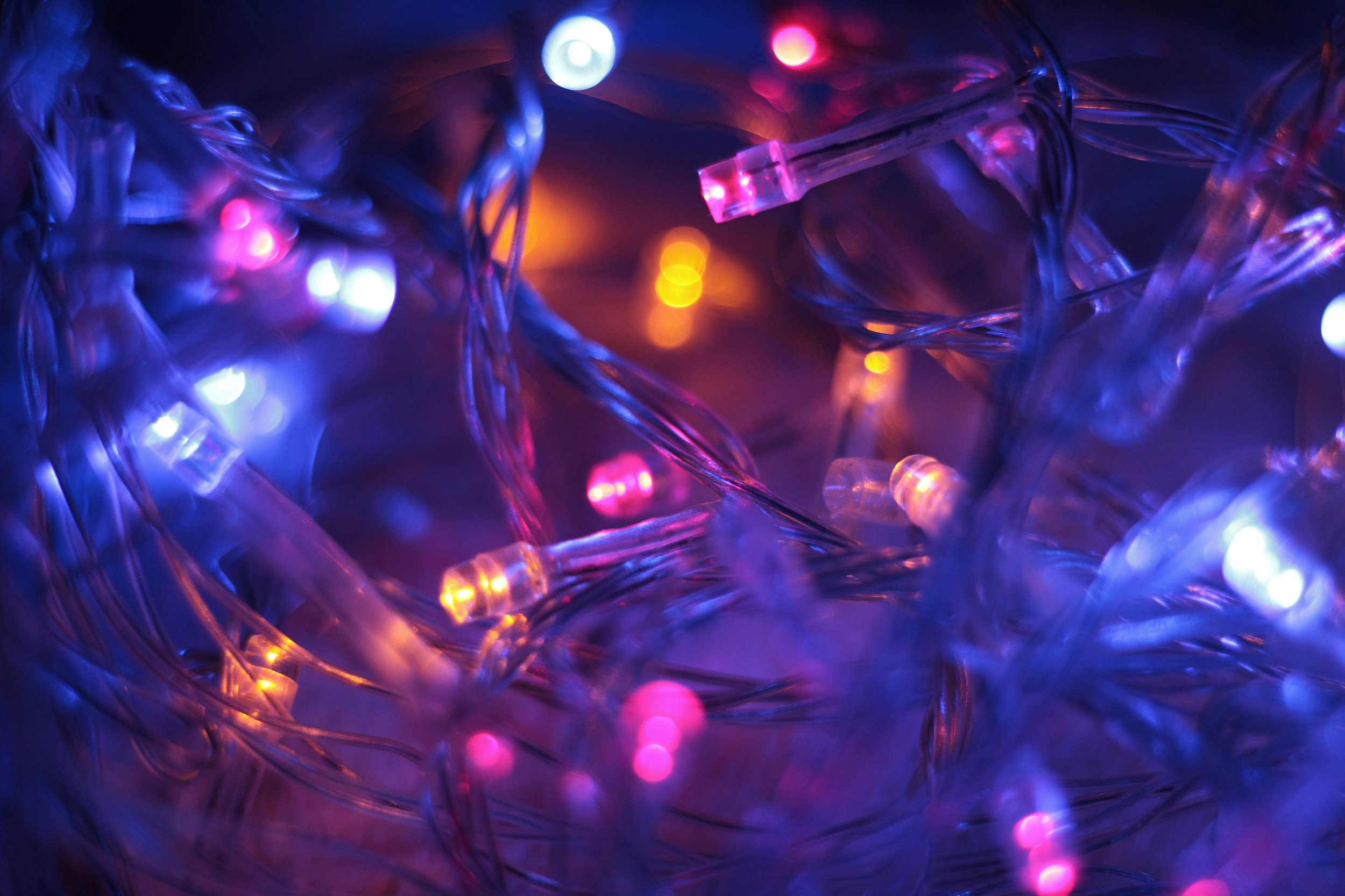 Close-up of multicolored LED string lights with purple, pink, blue, and orange glowing bulbs intertwined on a dark background.