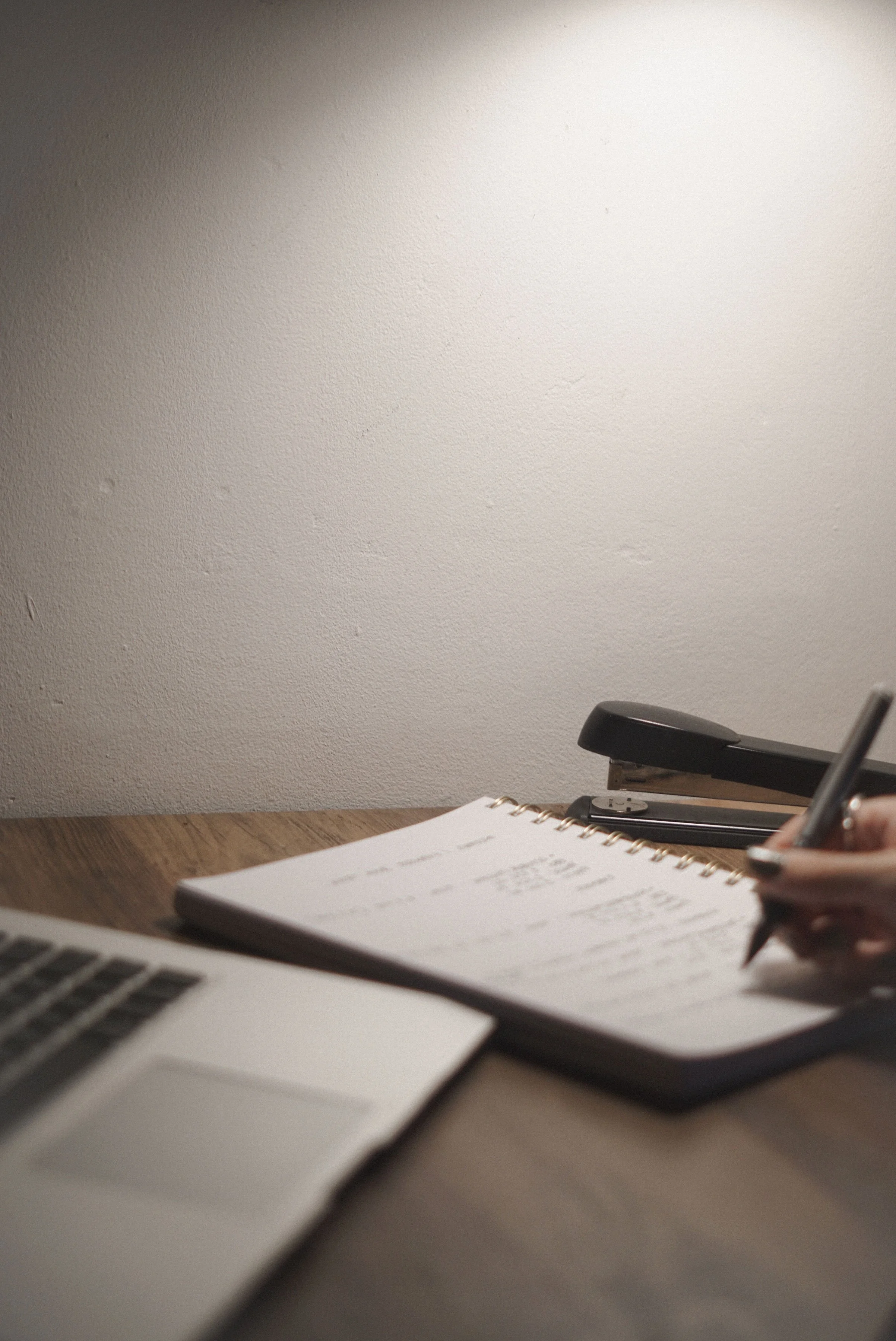 Wooden desk with closed black laptop, stacked spiral notebook, and iPad, representing wellness content for a therapist with virtual assistant support for digital product launches, content marketing, SEO, and admin