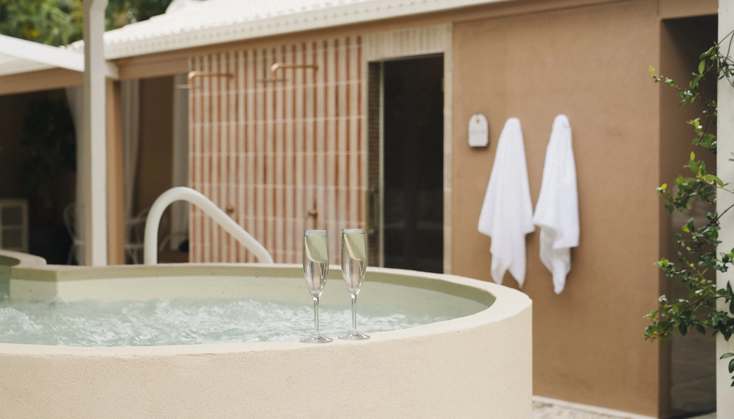 Red clay wall with bricks, two white towels, and white stone circular hot tub, representing a calming space for healers supported by a virtual assistant for digital launches, content marketing, SEO, and admin.