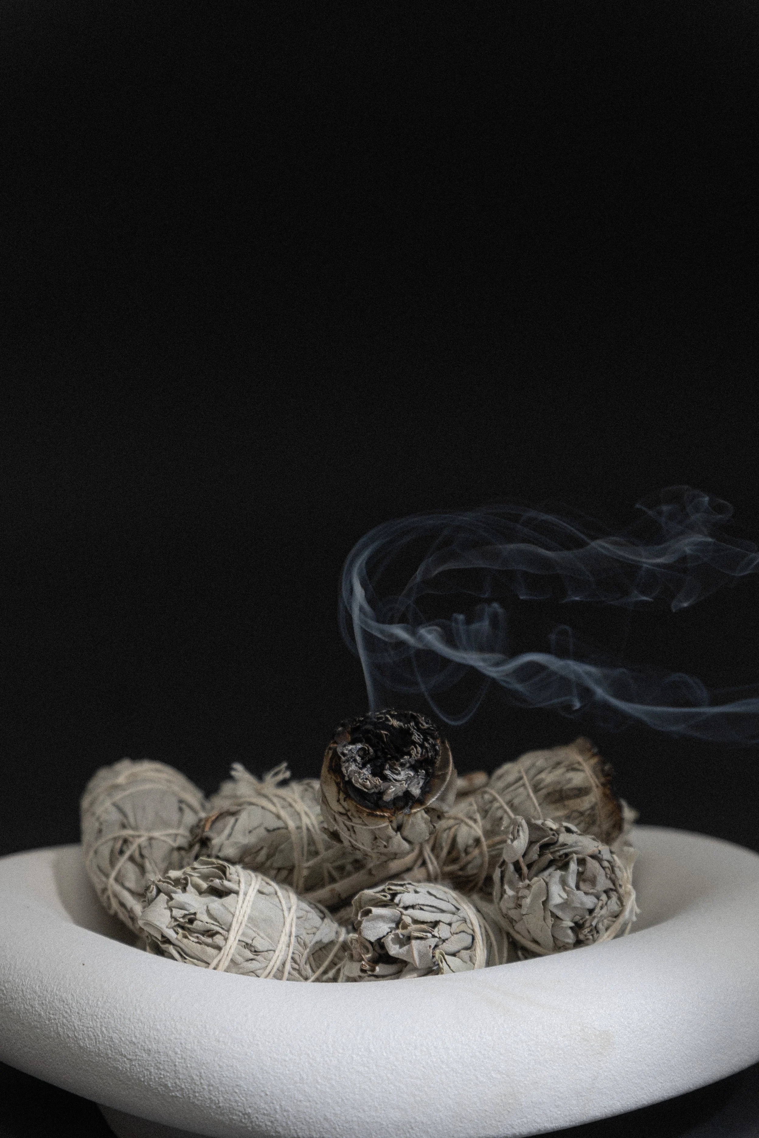 Bowl filled with sage smudge bundles, one actively burning, reflecting a healer’s calming workspace supported by virtual assistant help for digital product launches, marketing, SEO, and admin.