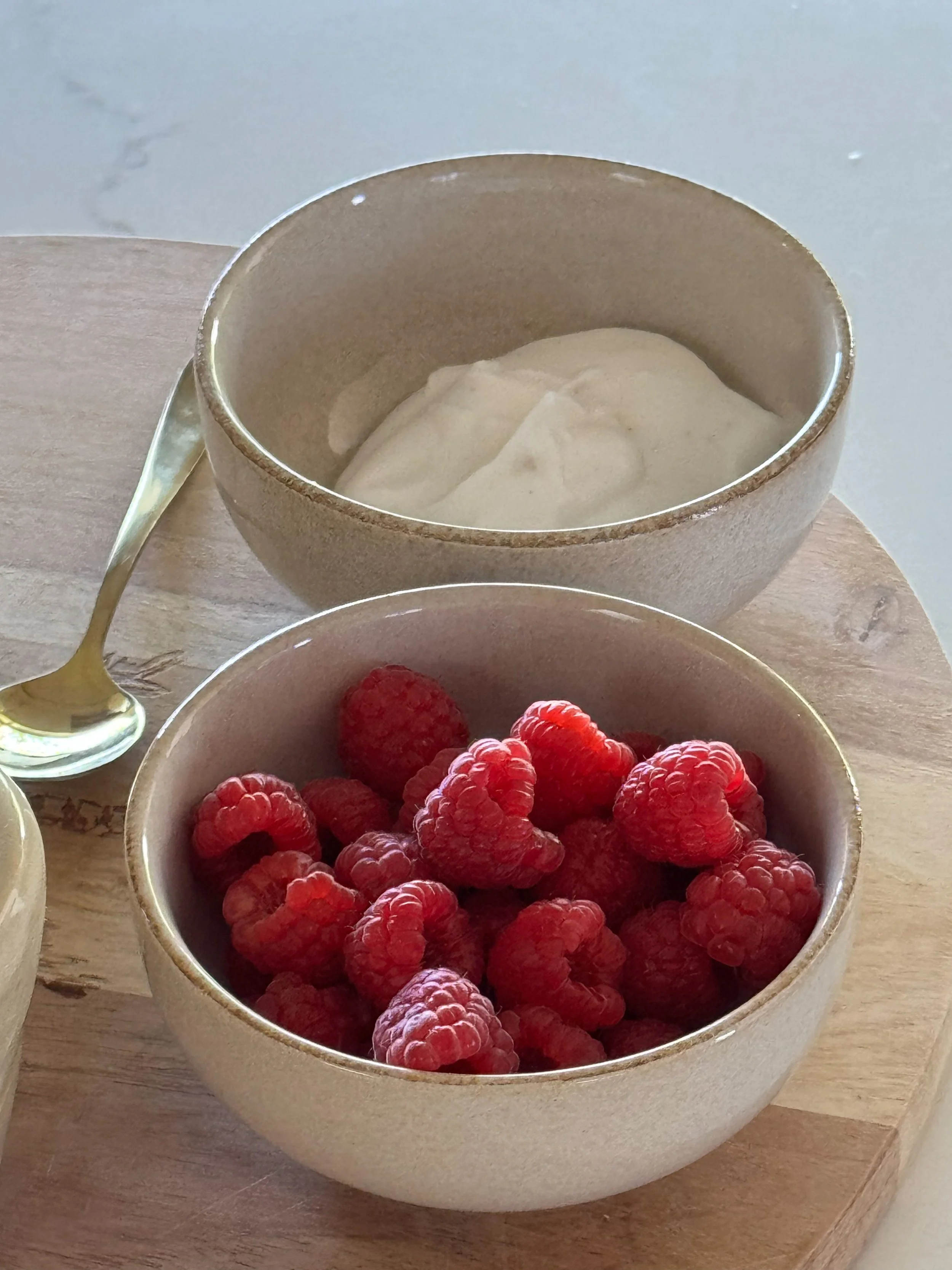 Two white ceramic bowls, one with fresh bright red raspberries and the other with white yogurt, representing nutrition-focused content created with virtual assistant support for SEO and digital product marketing.