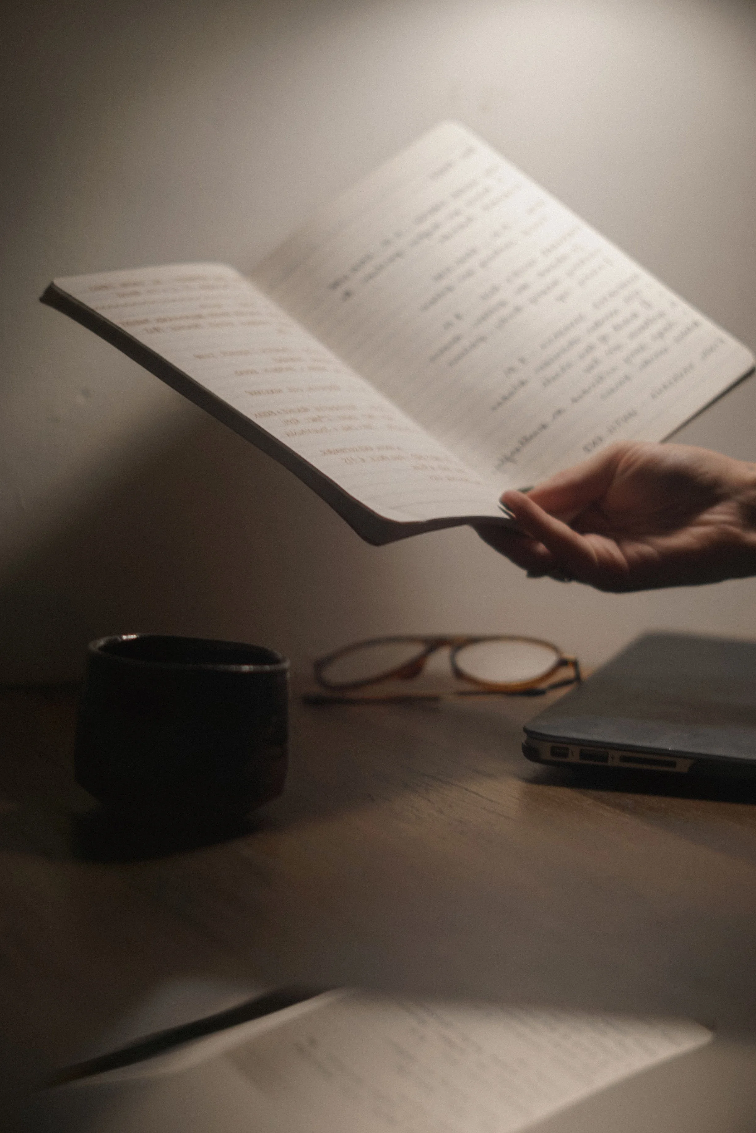 A dark wood desk belonging to a virtual assistant to life coaches; VA holds an open book oer the desk, where there is a notebook to the right and miscellaneous items to the left.