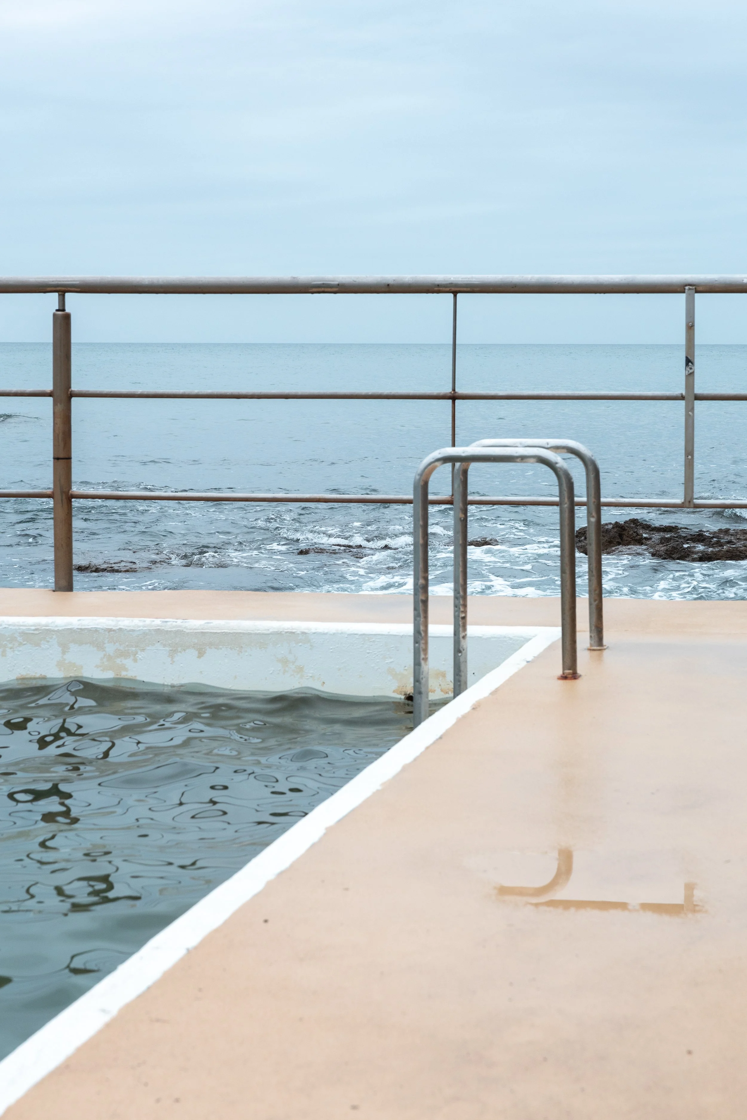 Outdoor pool with steel railing, concrete deck, and ladder overlooking the ocean, representing wellness content for a personal trainer with virtual assistant support for digital product launches, content marketing, SEO, and admin services