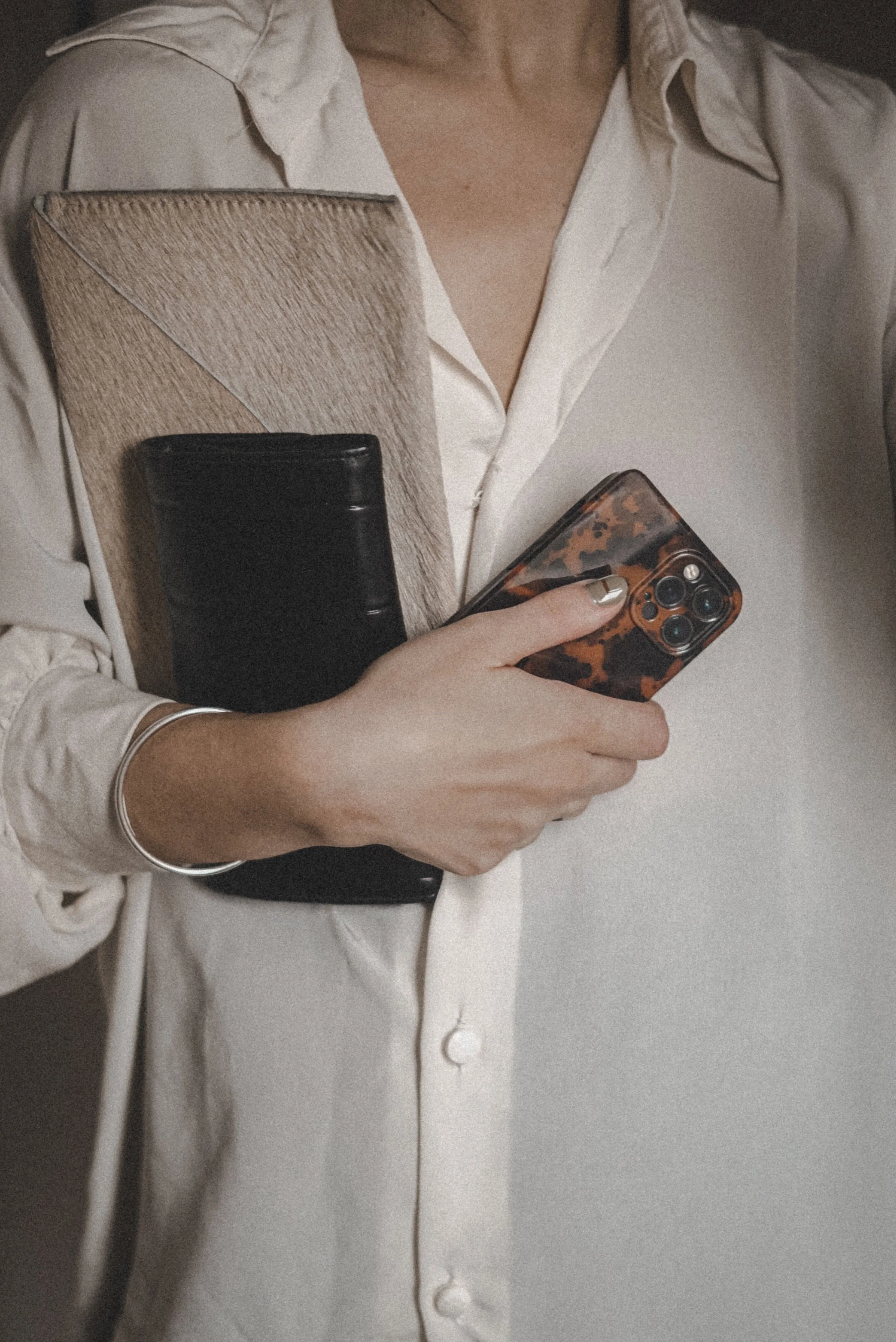 Woman in white linen blouse holding cream folder and black notebook with one arm and phone in the other, representing wellness content for a therapist with virtual assistant support for digital product launches, content marketing, SEO, and admin