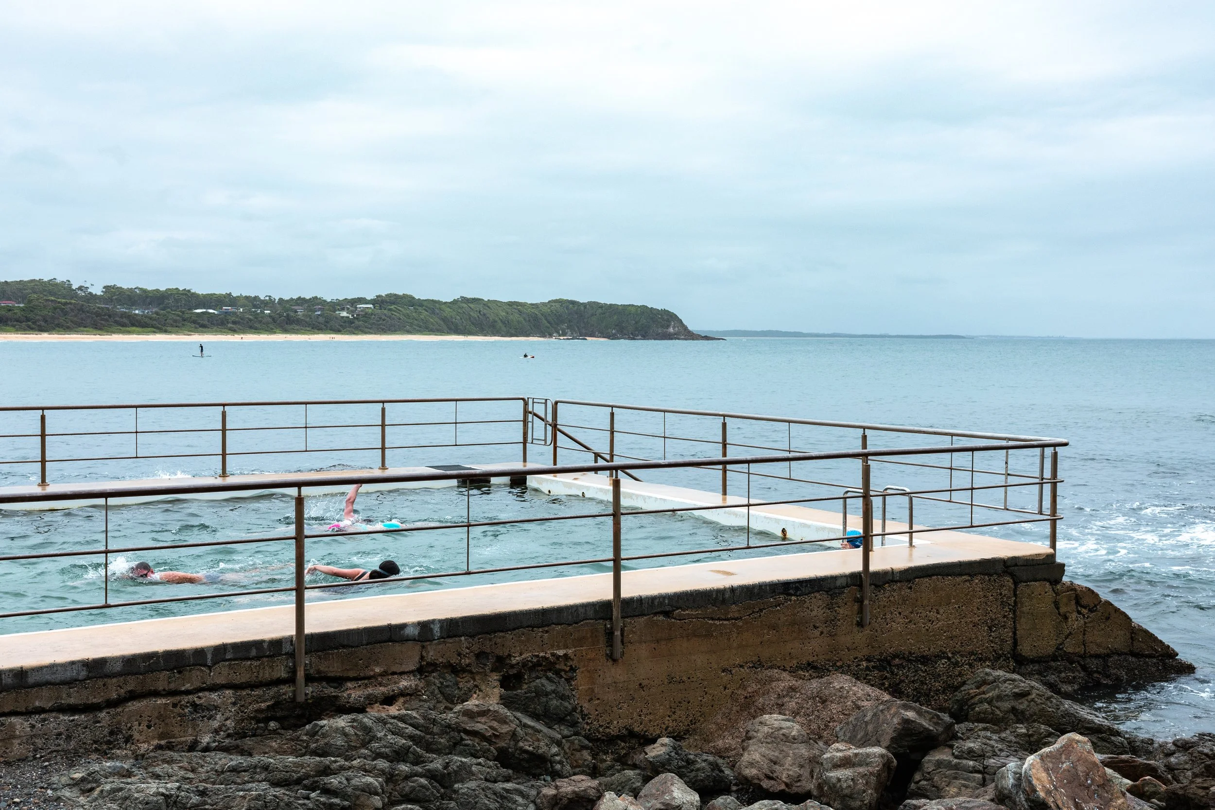 Overview of an outdoor pool next to the ocean with rocks in the foreground, representing wellness copywriting and content for personal trainers, supported by virtual assistant services for digital product launches, content marketing, SEO, and admin.