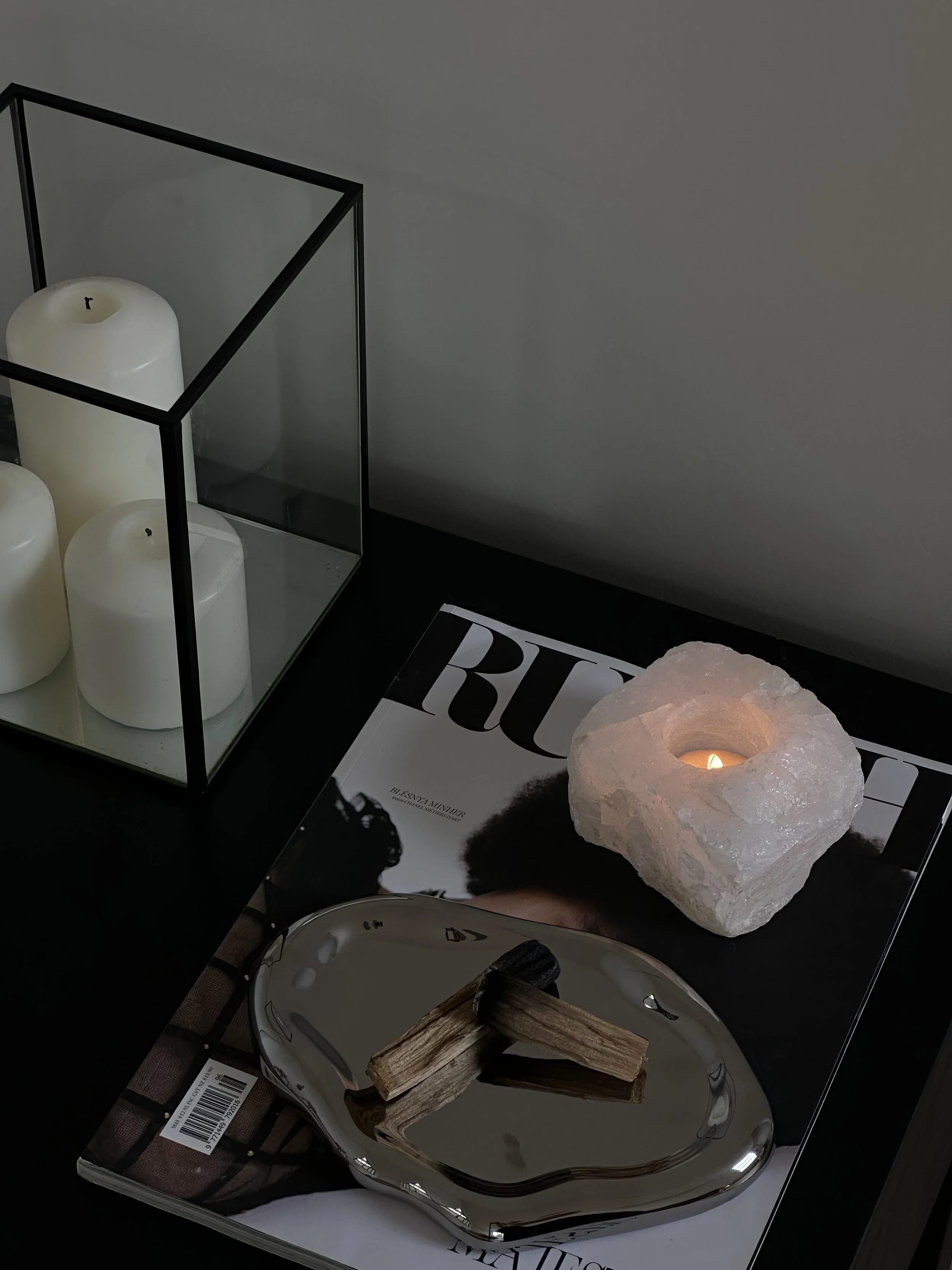 Table with palo santo, a magazine, a lit crystal candle, and a glass vase holding three white pillar candles, reflecting the calming aesthetic of healers supported by VA services for launches, marketing, SEO, and admin.