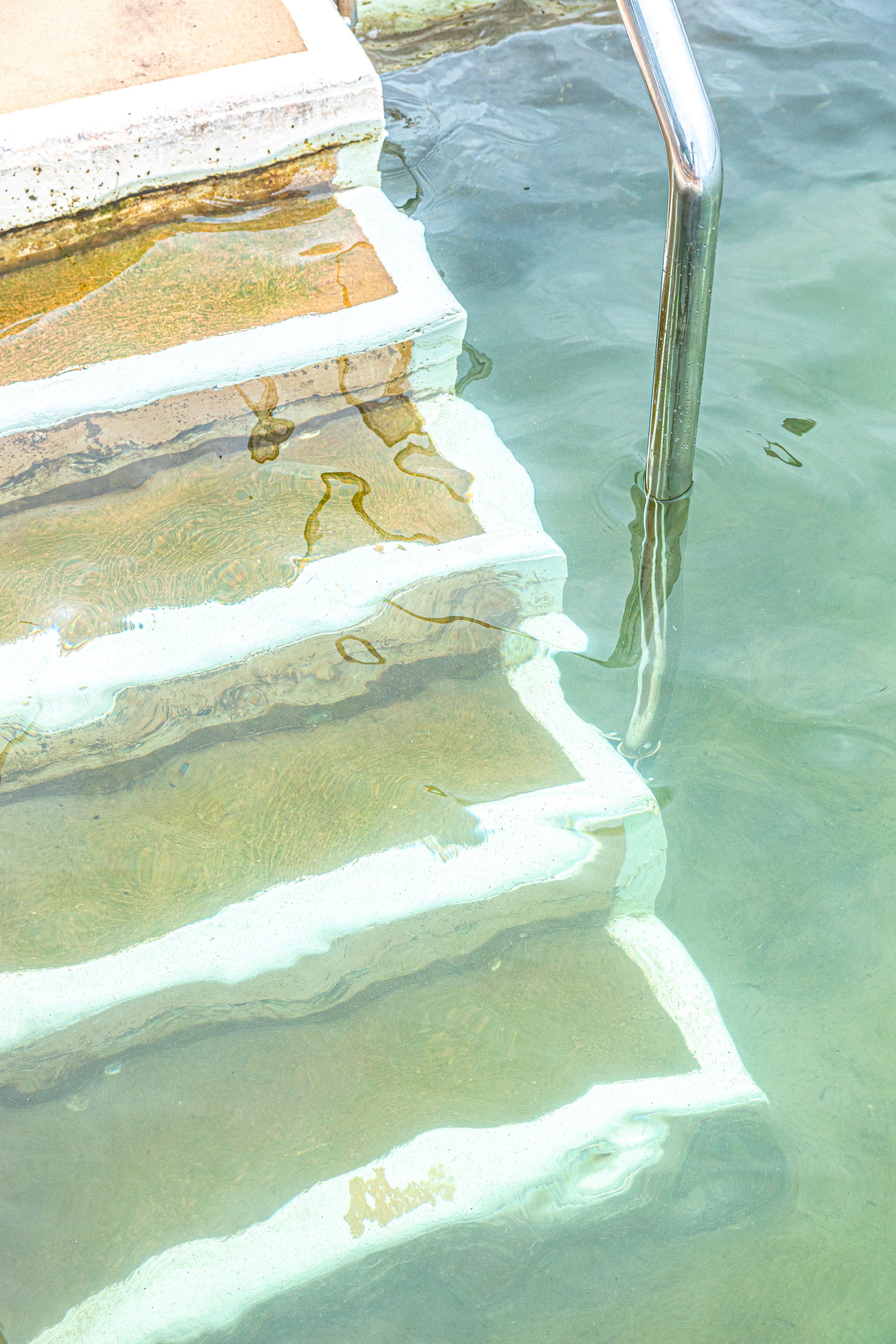 Concrete stairs with steel railing leading into an outdoor pool, representing wellness copywriting and content for personal trainers, supported by virtual assistant services for digital product launches, content marketing, SEO, and admin.