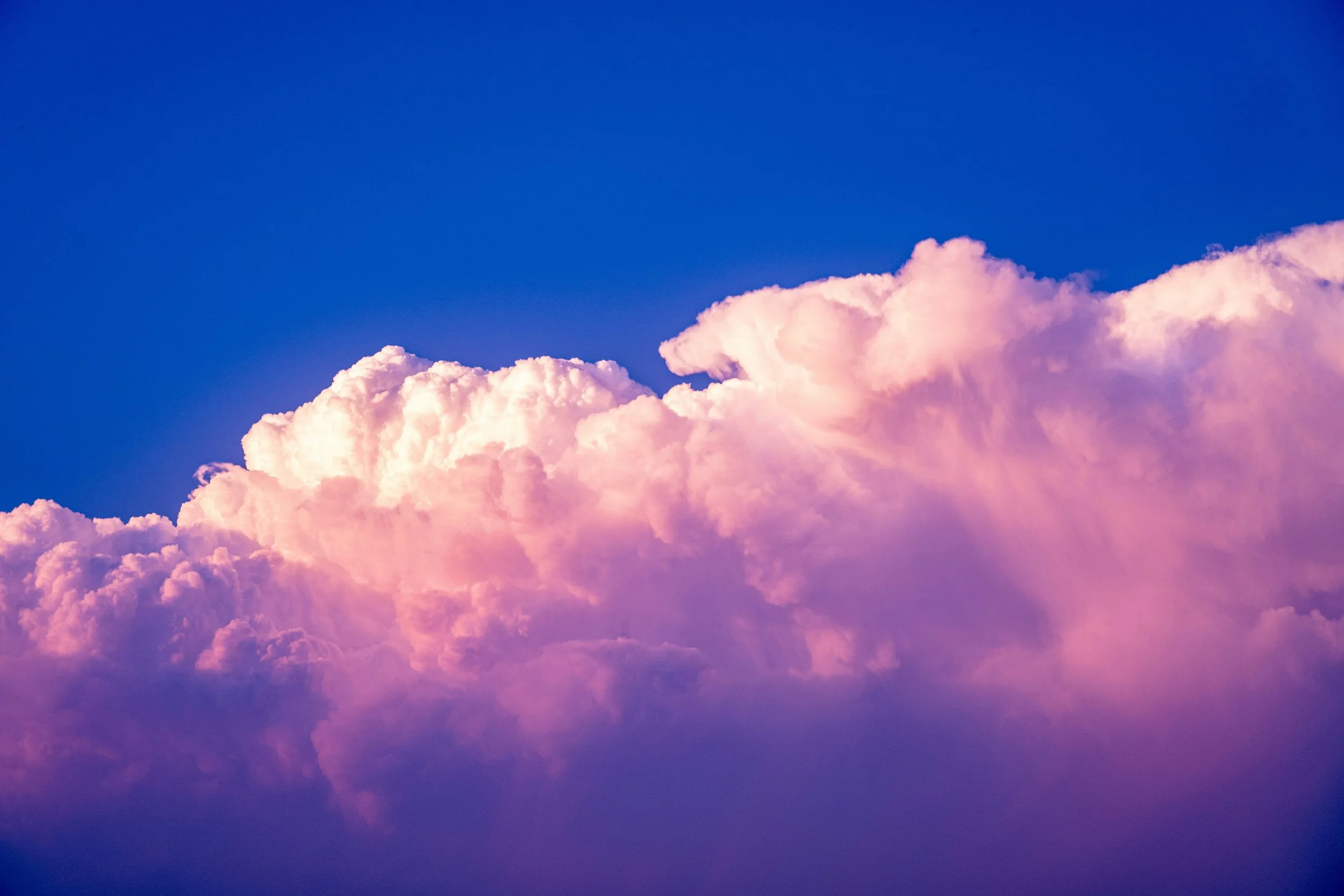 Towering pink and white cumulus clouds lit by sunset against a deep blue sky, representing momentum building behind successful launches.
