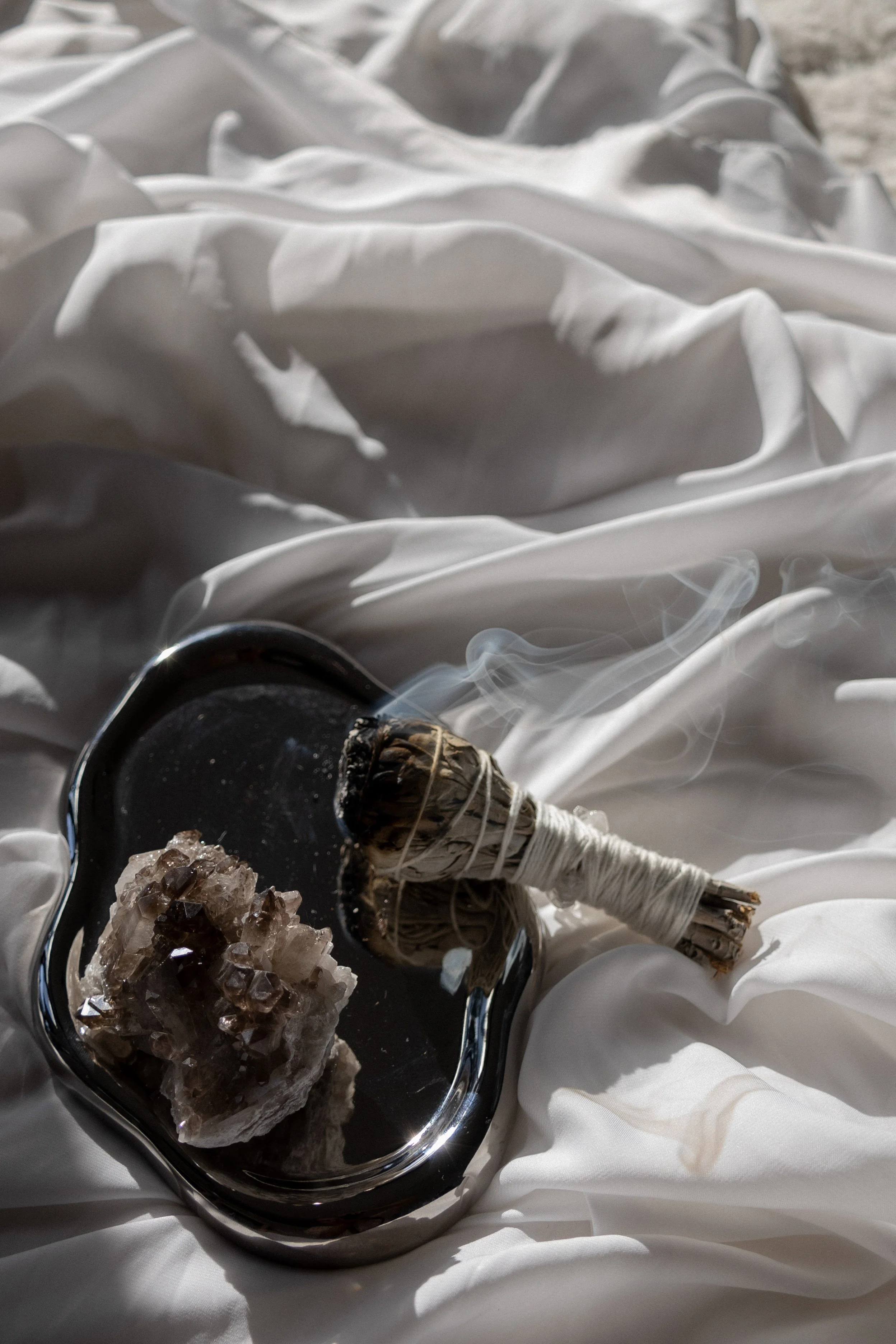 Silver tray on white silk cloth holding a purple crystal and burning sage smudge, representing a healer’s calming workspace supported by virtual assistant services for digital product launches, content marketing, SEO, and admin.