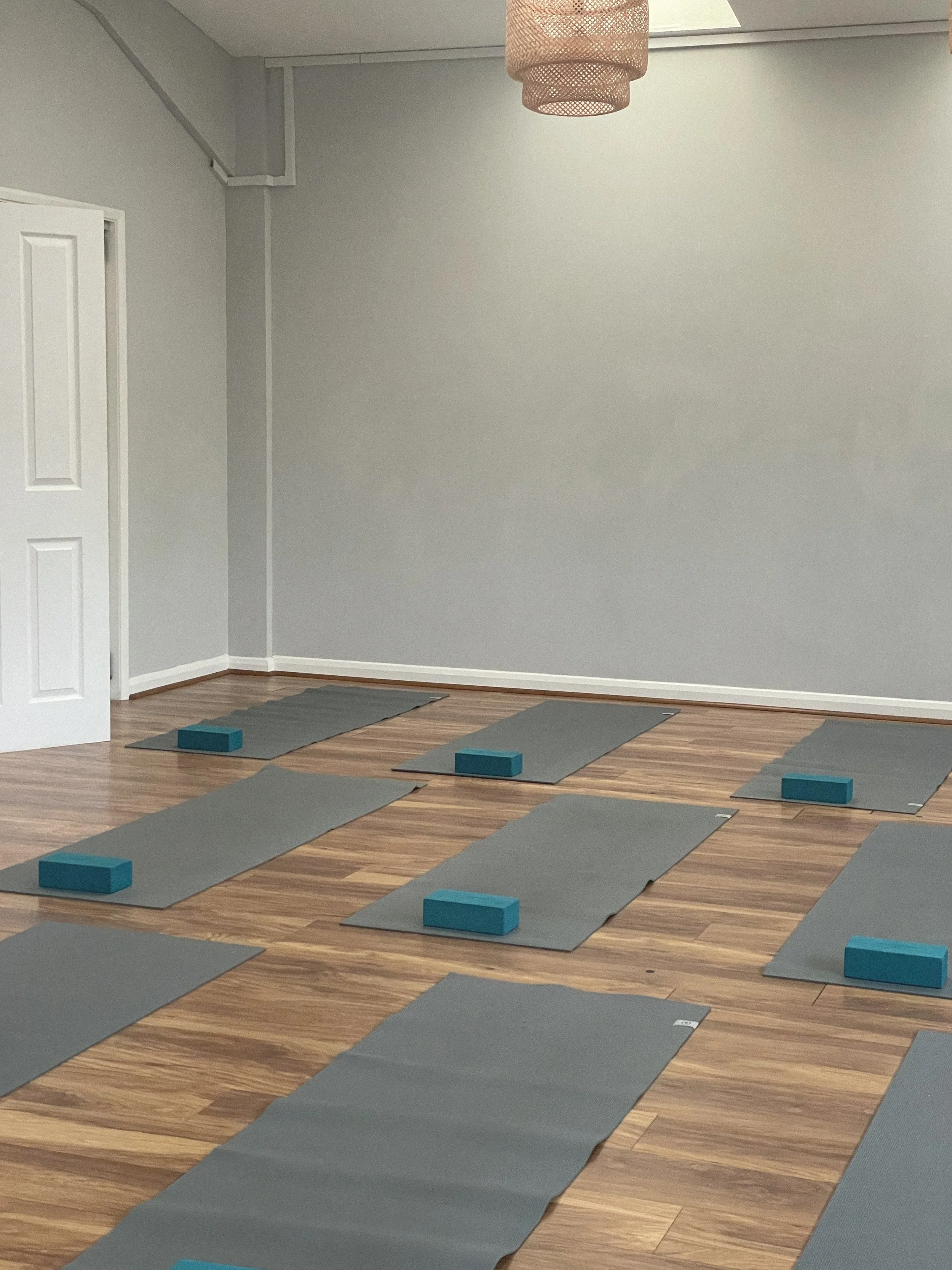 Grey yoga mat on a wooden Pilates studio floor with cork yoga blocks, grey foam pad, and grey dumbbells, representing fitness and wellness content created with virtual assistant support for digital products, content marketing, and SEO.