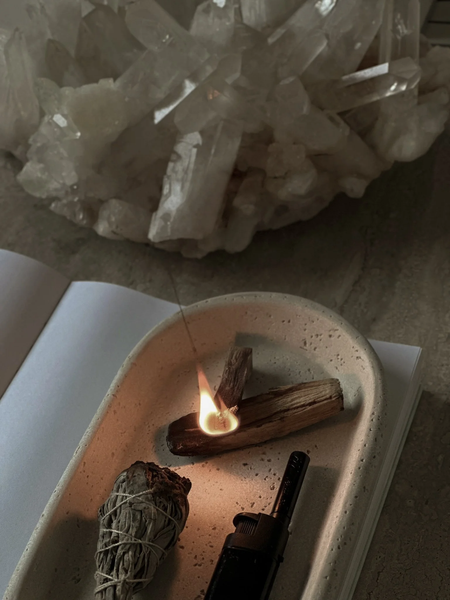 Oblong stone tray with burning palo santo, unburned sage smudge, and a white crystal beside it, representing a healer’s wellness space supported by virtual assistant services for launches, content marketing, SEO, and admin.