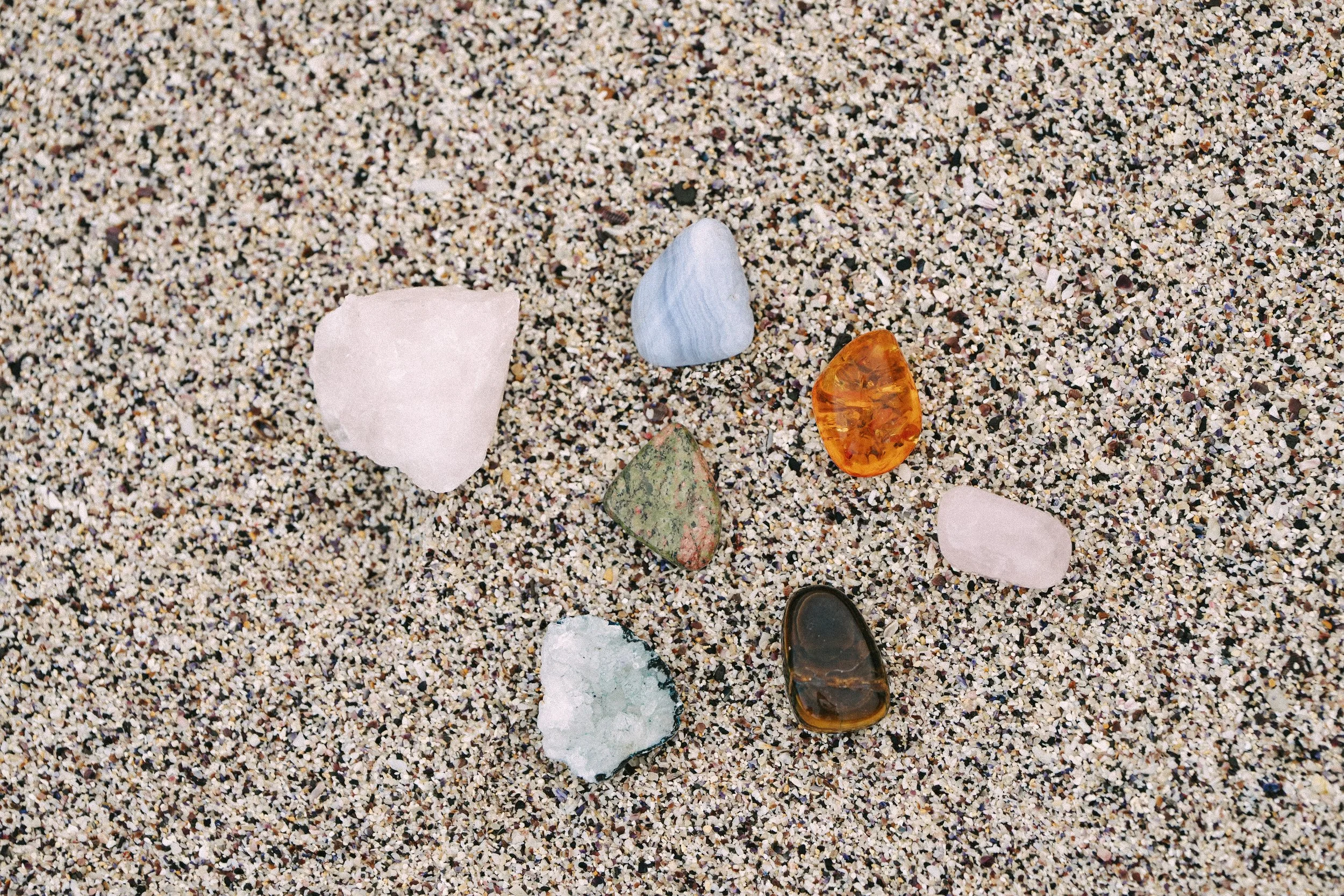 Multicolored crystals and stones scattered in sand, symbolizing a healer’s calming space supported by virtual assistant services for digital product launches, content marketing, SEO, and admin.