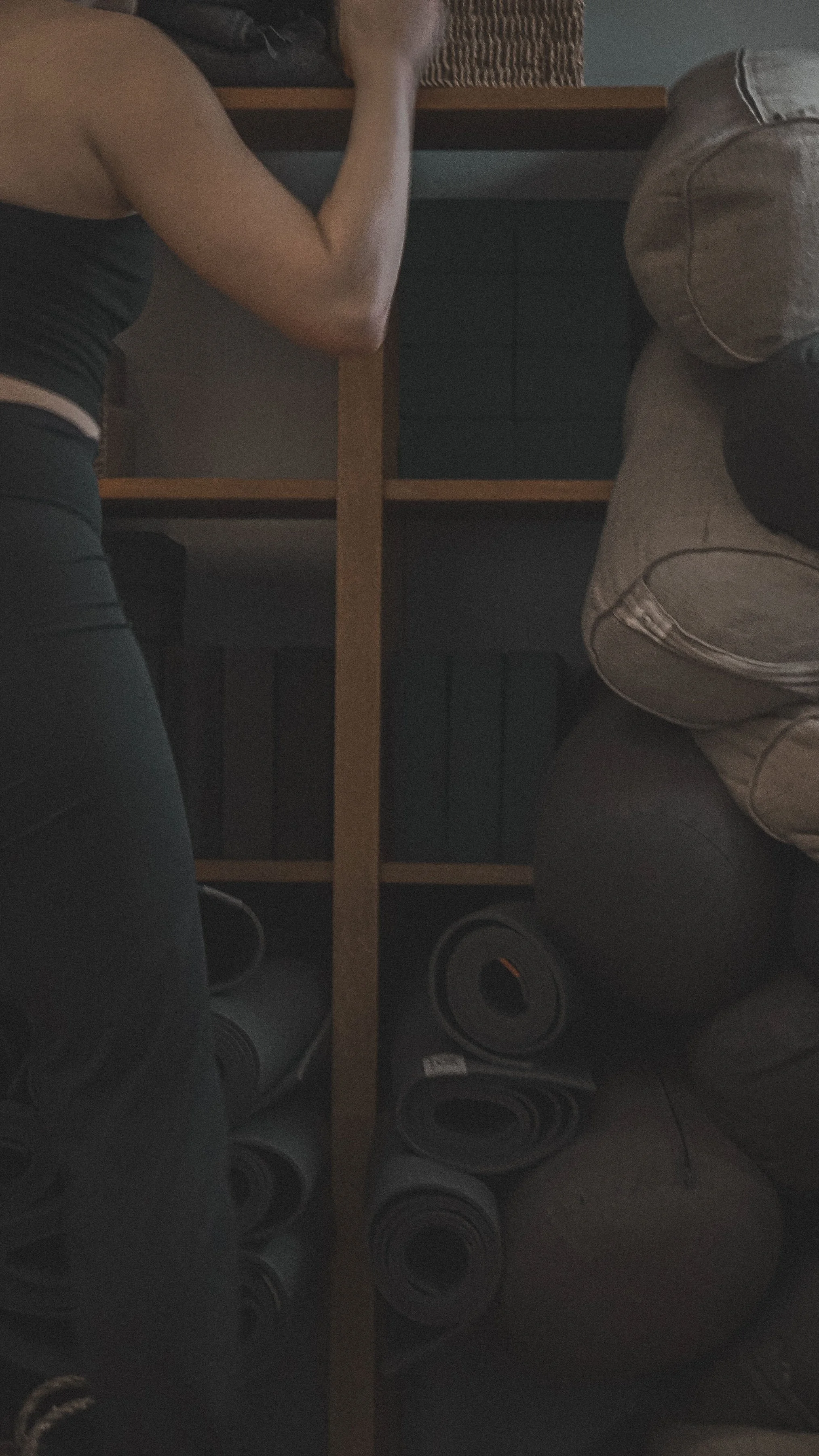 Yoga practitioner in black standing in front of a studio shelf holding yoga blocks, bolsters, and mats, representing fitness and wellness content created with virtual assistant support for digital products, content marketing, and SEO