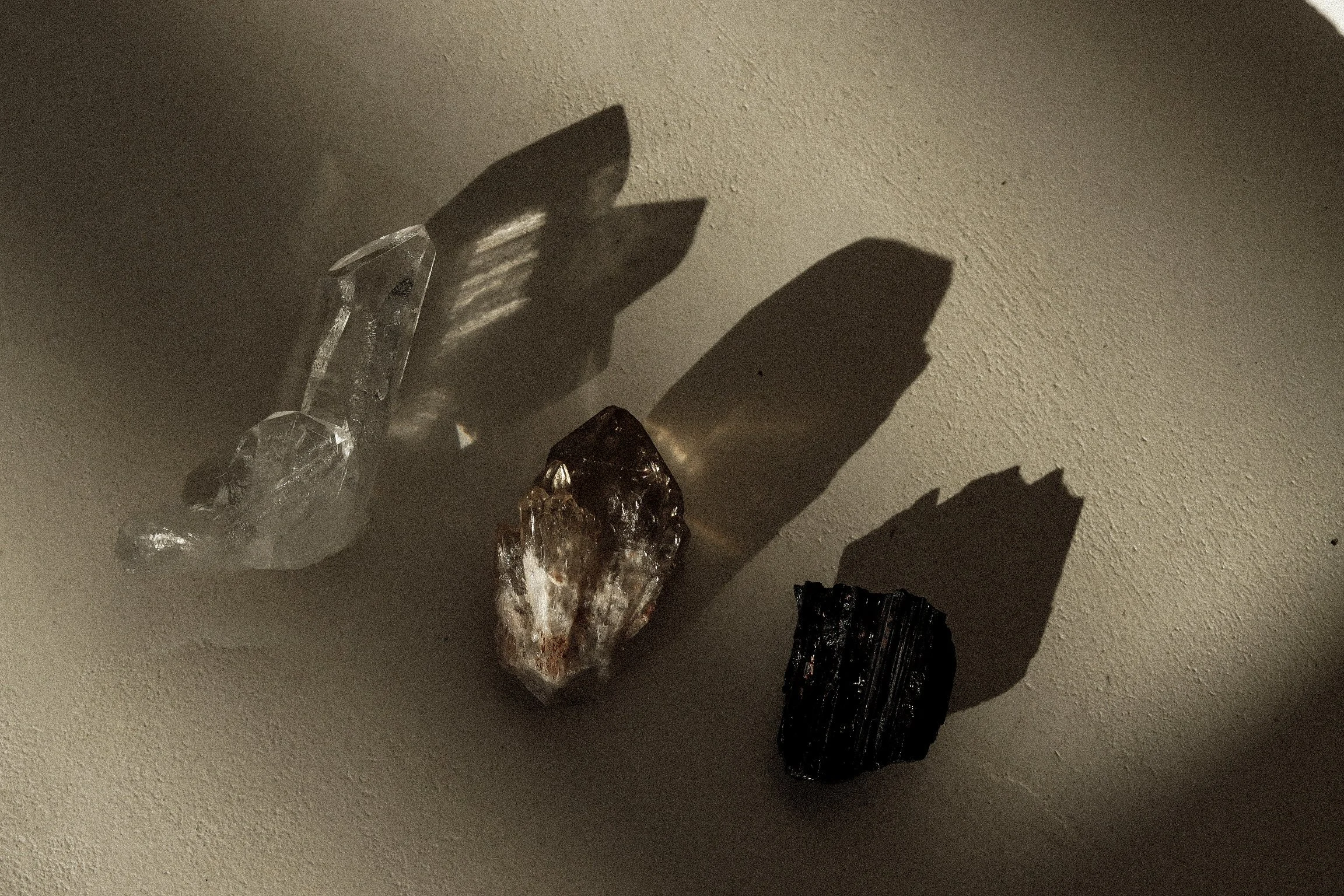 Three crystals lined up on white concrete table, reflecting a healer’s workspace supported by virtual assistant services for digital product launches, content marketing, SEO, and admin.