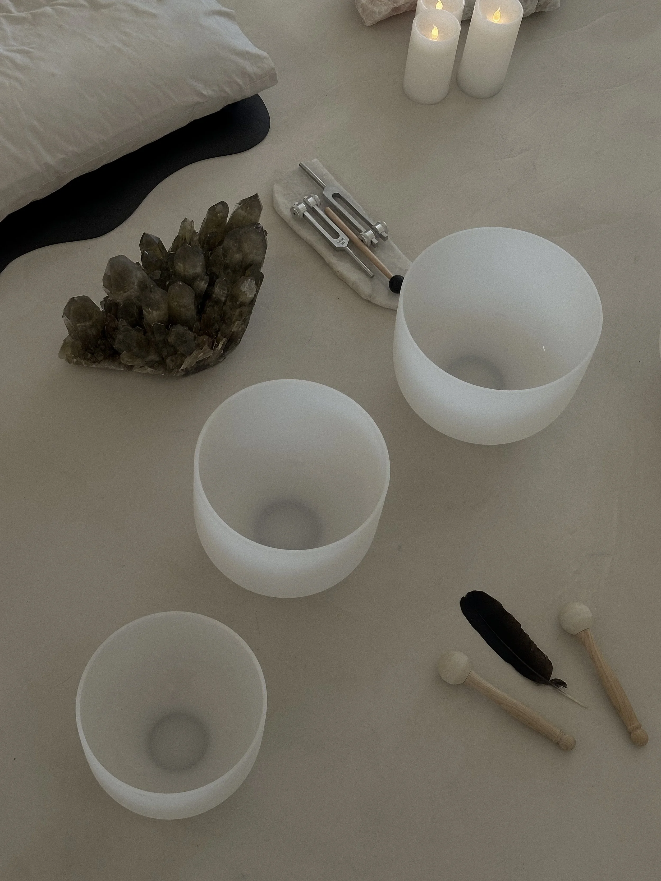 three white sound bath bowls with dark crystal and feather on white floor, reflecting the depth of wellness practitioner expertise that Azure Small Business Solutions helps package and launch as online courses