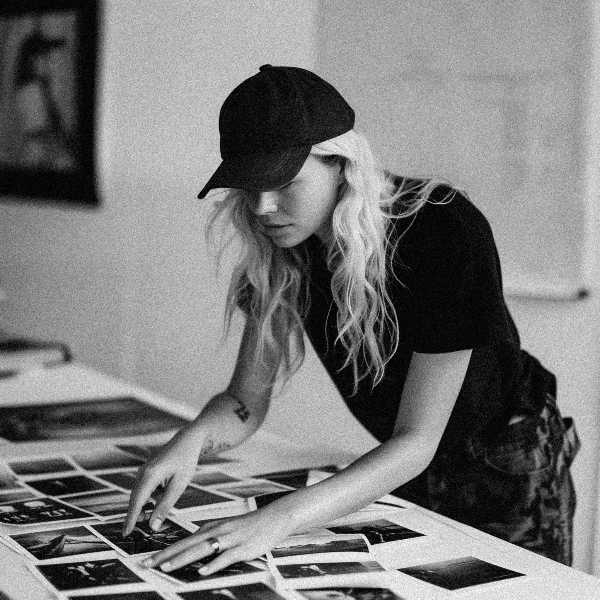 woman in black ball cap reviewing images on a table, reflecting the strategic, detail-oriented approach behind content marketing and social media management for health and wellness coaches