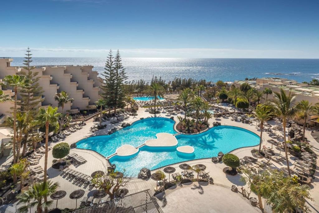 Hotelanlage mit Pool, Palmen und Blick auf das Meer.