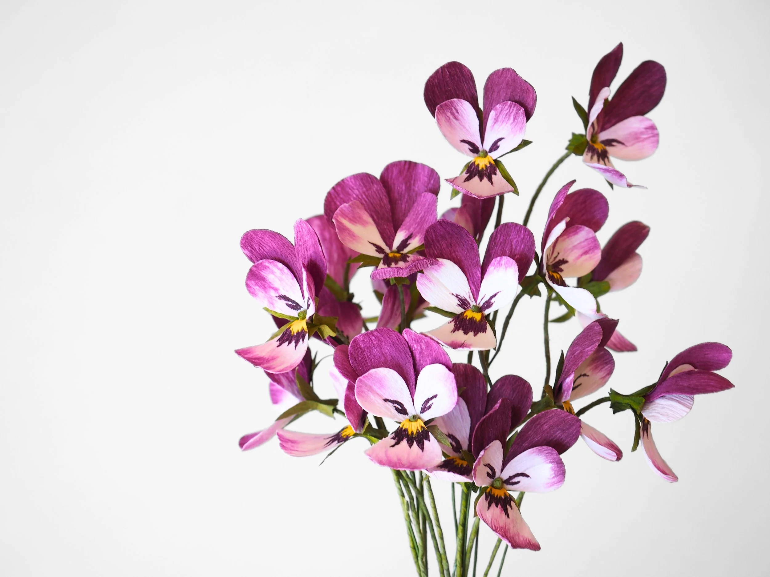 A bouquet of purple, pink, and white painted flowers with green stems against a white background.
