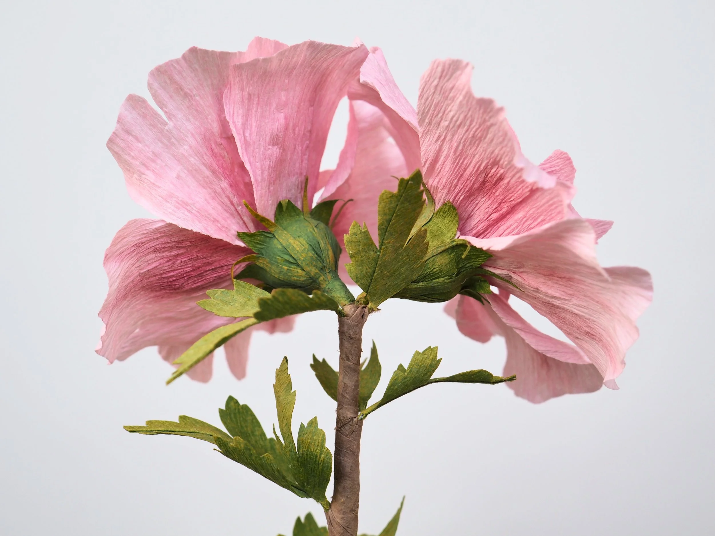Artificial pink flower with green leaves on a gray background.