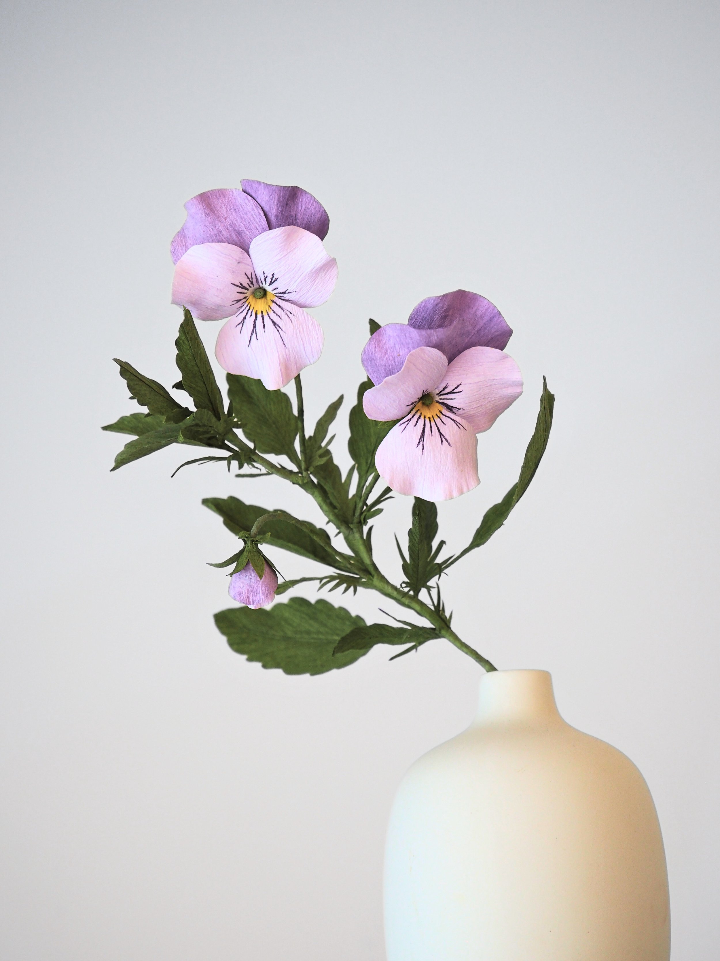 A white vase with a bunch of pink and purple flowers with green leaves.
