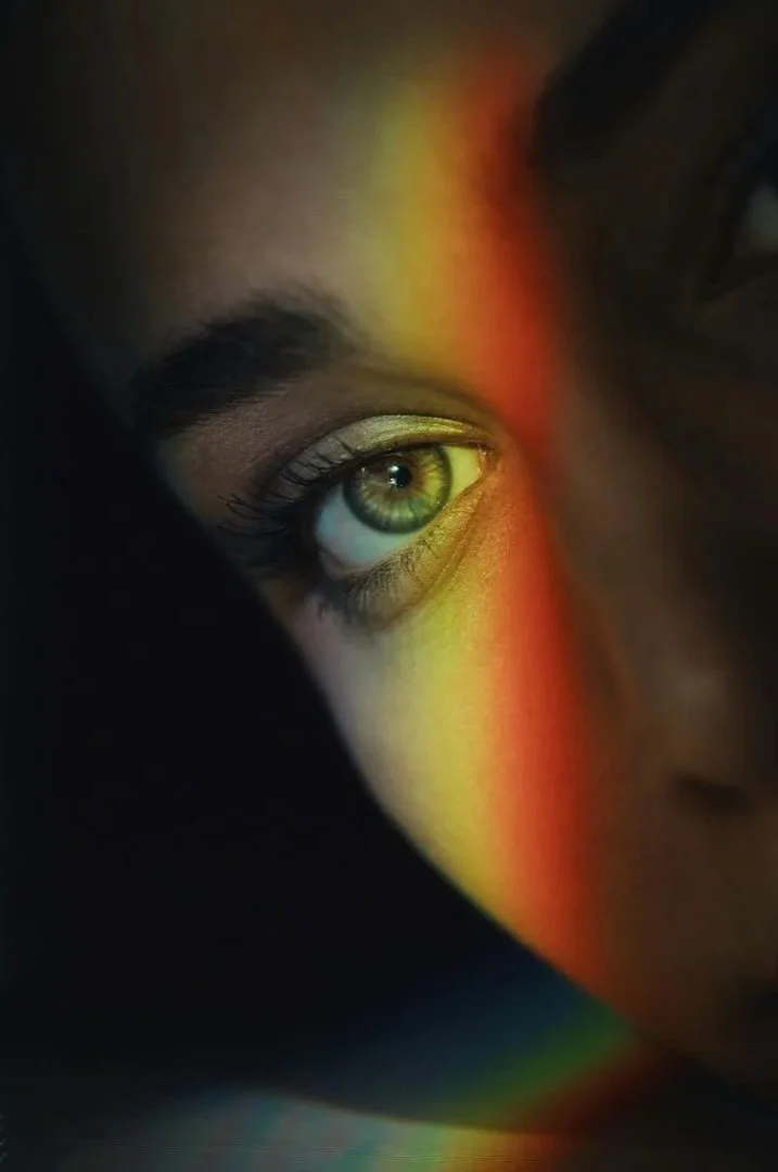 Close-up of a person's eye with a rainbow spectrum of light cast across their face.