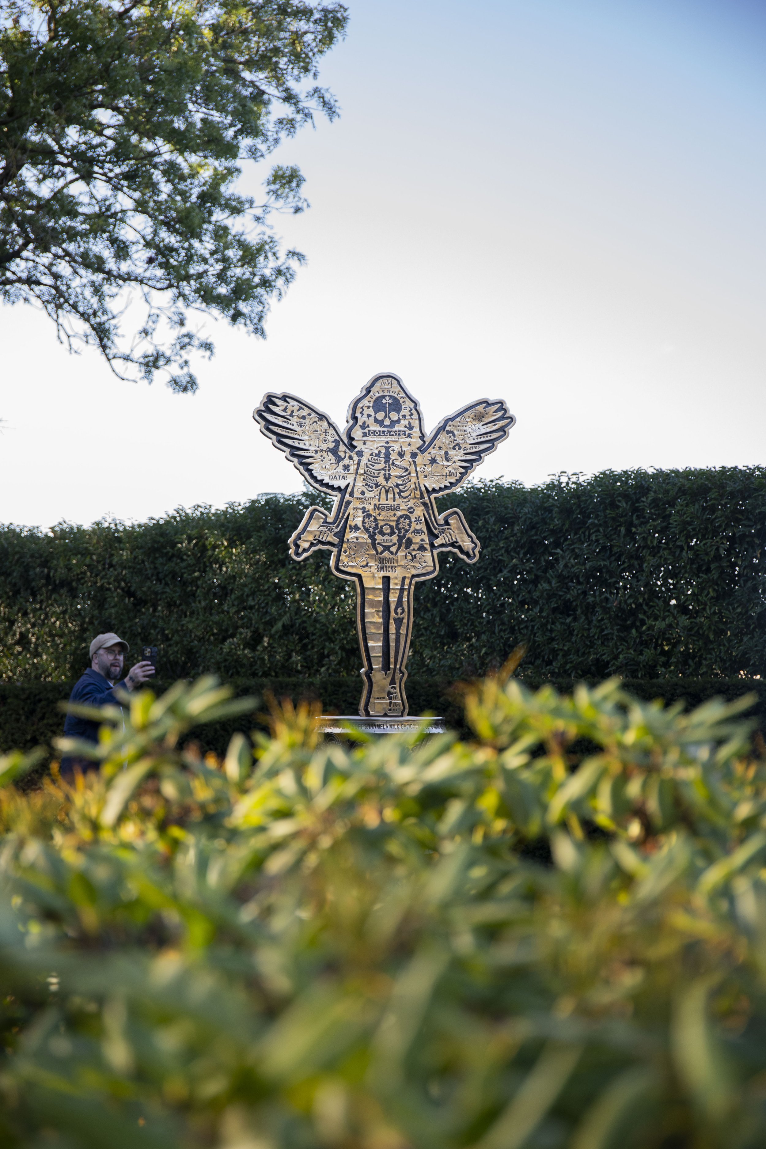Monumental Angel Cake bronze sculpture by British artist Lhouette installed in a private garden, featuring the full winged figure rising above a bronze oil drum.