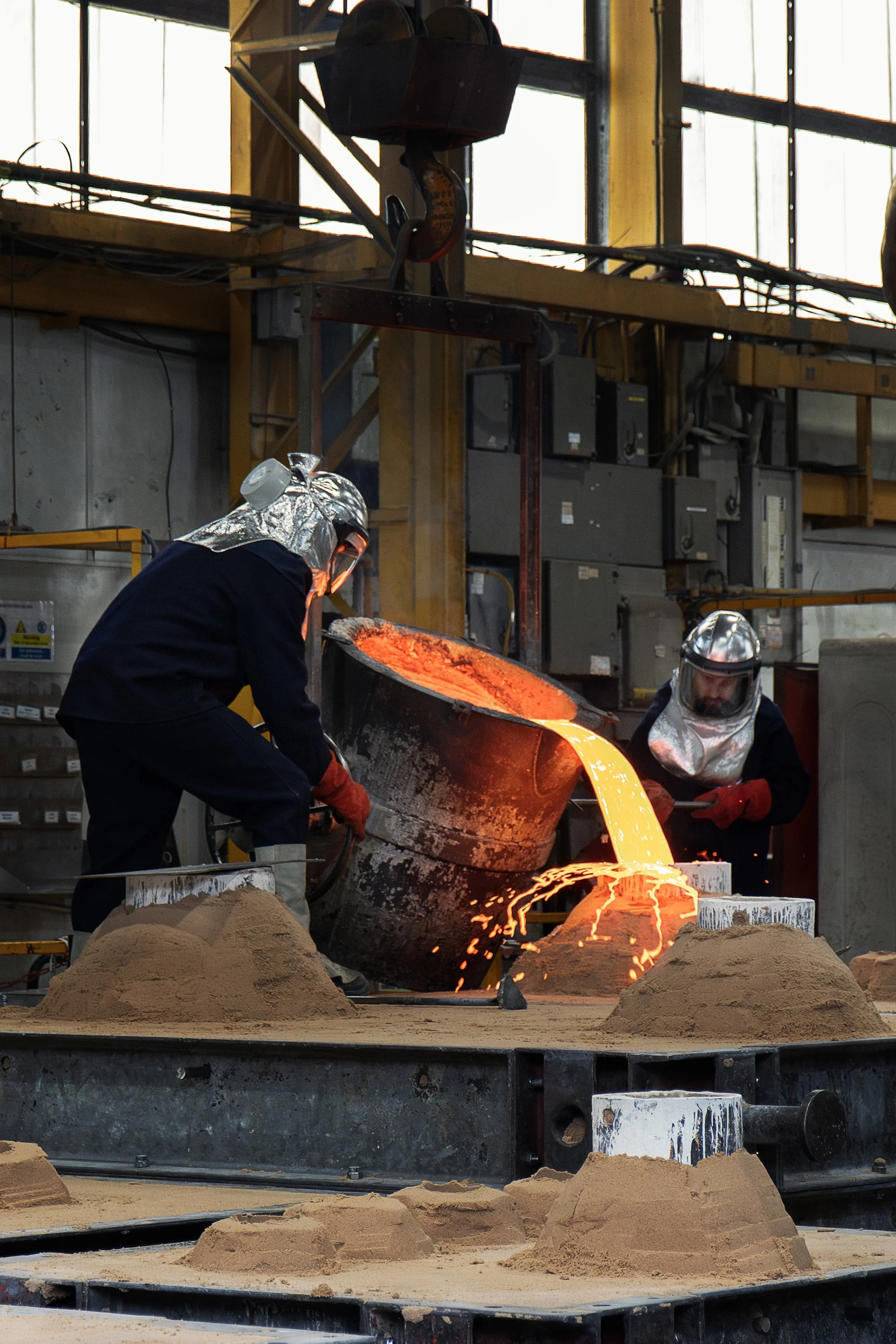 Pangolin Editions foundry workers wearing full protective equipment pouring molten bronze into a casting mould during the traditional bronze sculpture production process.