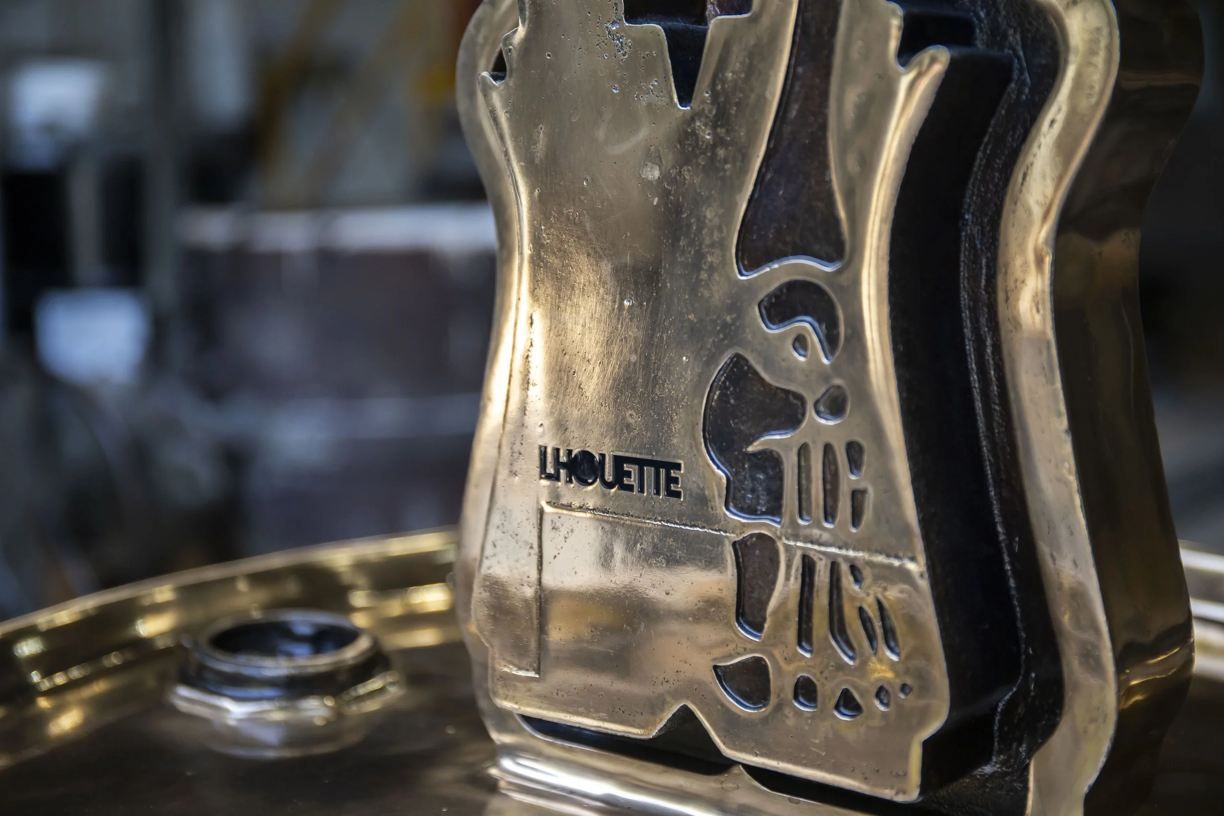 Close-up of the Lhouette artist signature cast into the bronze surface of A Fall from Grace – Angel Cake, showing the sculpture's textured metal finish.