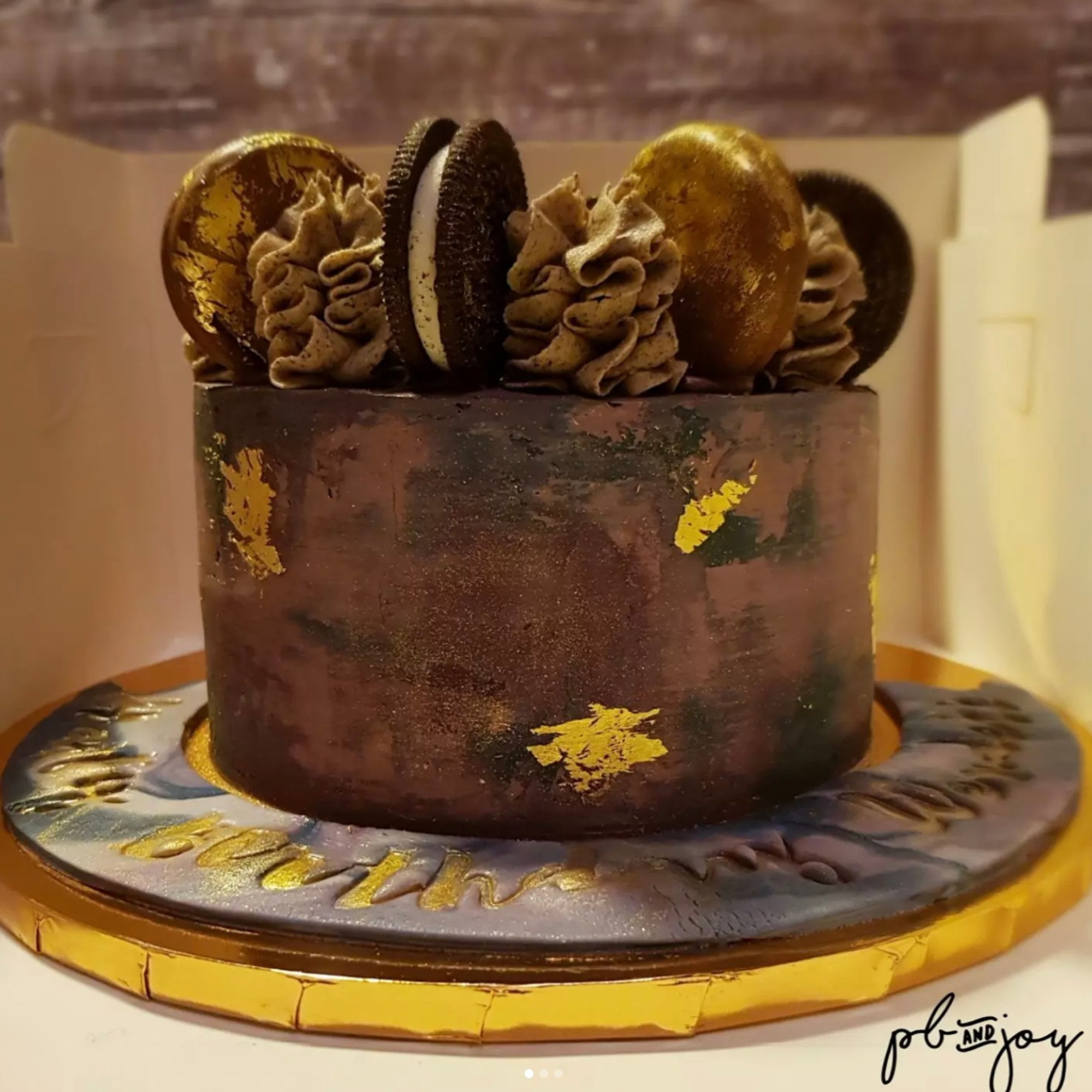 Chocolate cake decorated with gold accents, cookies, and chocolate frosting on top.