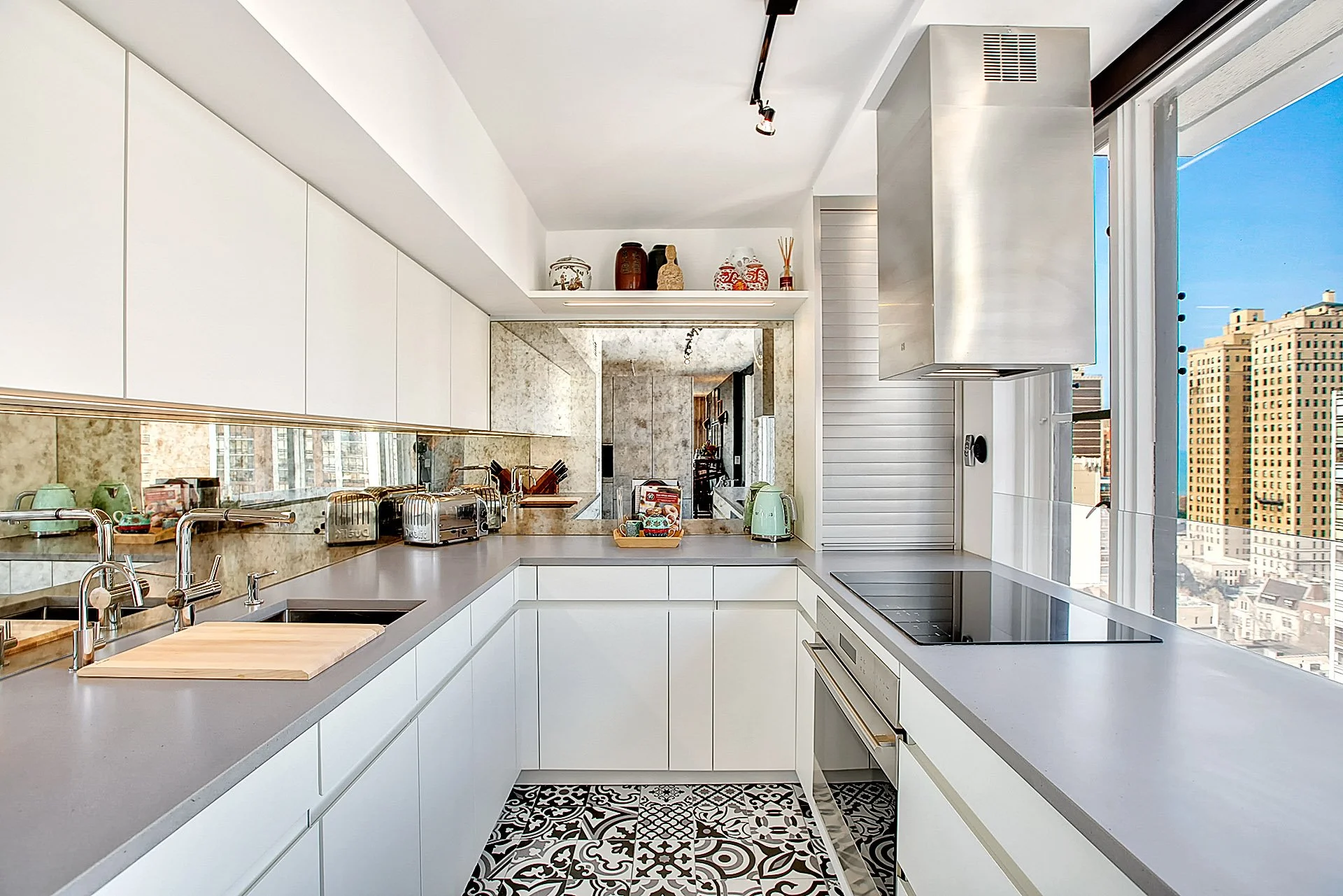 Modern white kitchen with countertops, stove, and a city view through large windows.