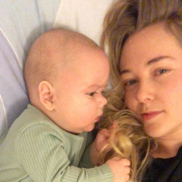 A young woman lying down next to a small child with a bun hairstyle, both looking at each other, in a close-up selfie.