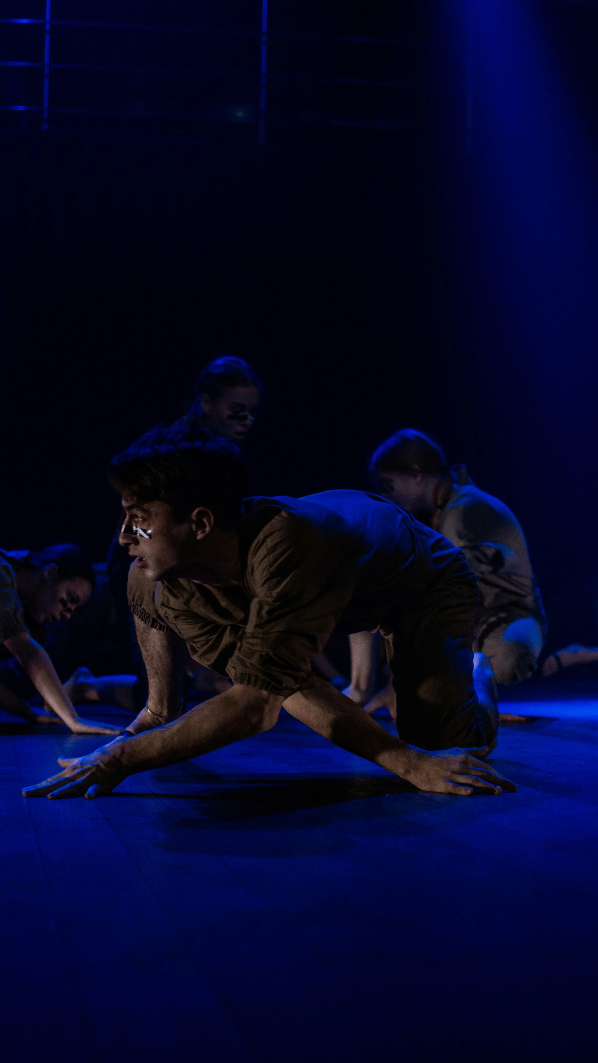 People performing a dance or yoga routine on a dark stage illuminated with blue lighting.