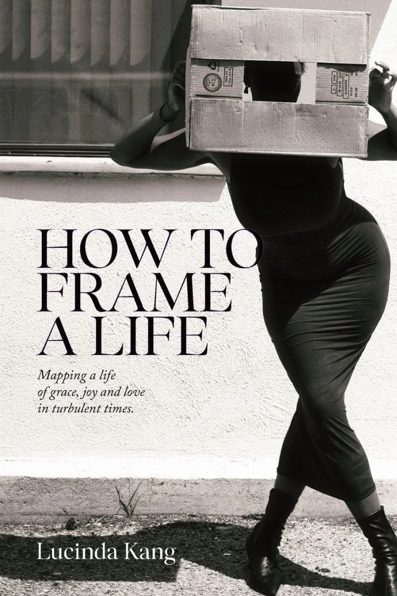 Book cover titled "How to Frame a Life" showing a woman in dark clothing carrying a cardboard box on her head, standing against a textured wall and window, with the subtitle "Mapping a life of grace, joy and love in turbulent times" and author's name Lucinda Kang.
