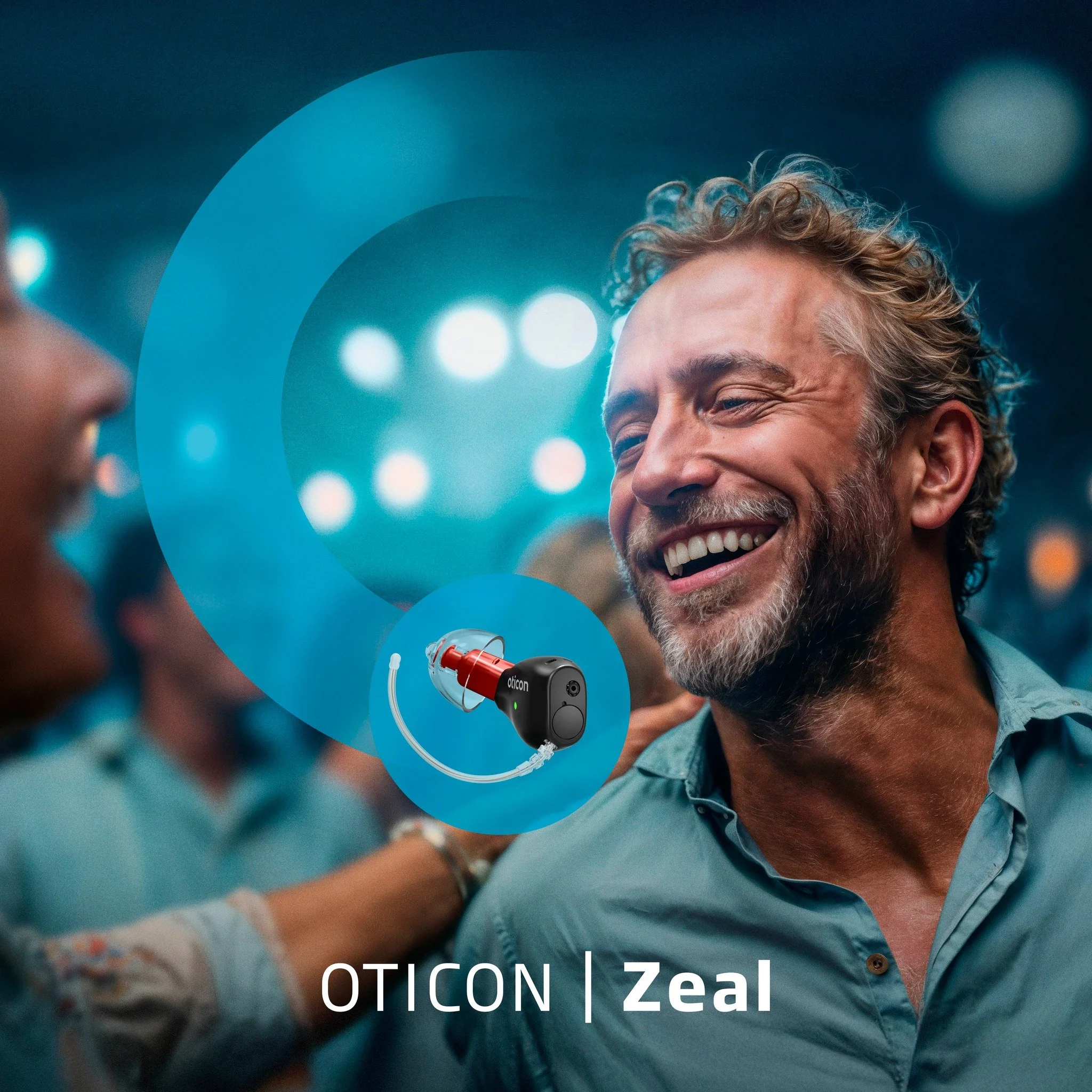 A man smiling and talking at a party or social gathering with a woman, with a hearing device and a digital graphic overlay indicating hearing aid technology called OTICON Zeal.