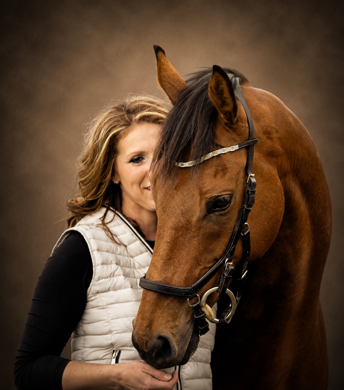 A woman with light brown hair smiling and hugging a brown horse with a shiny coat and black mane, against a brown gradient background.