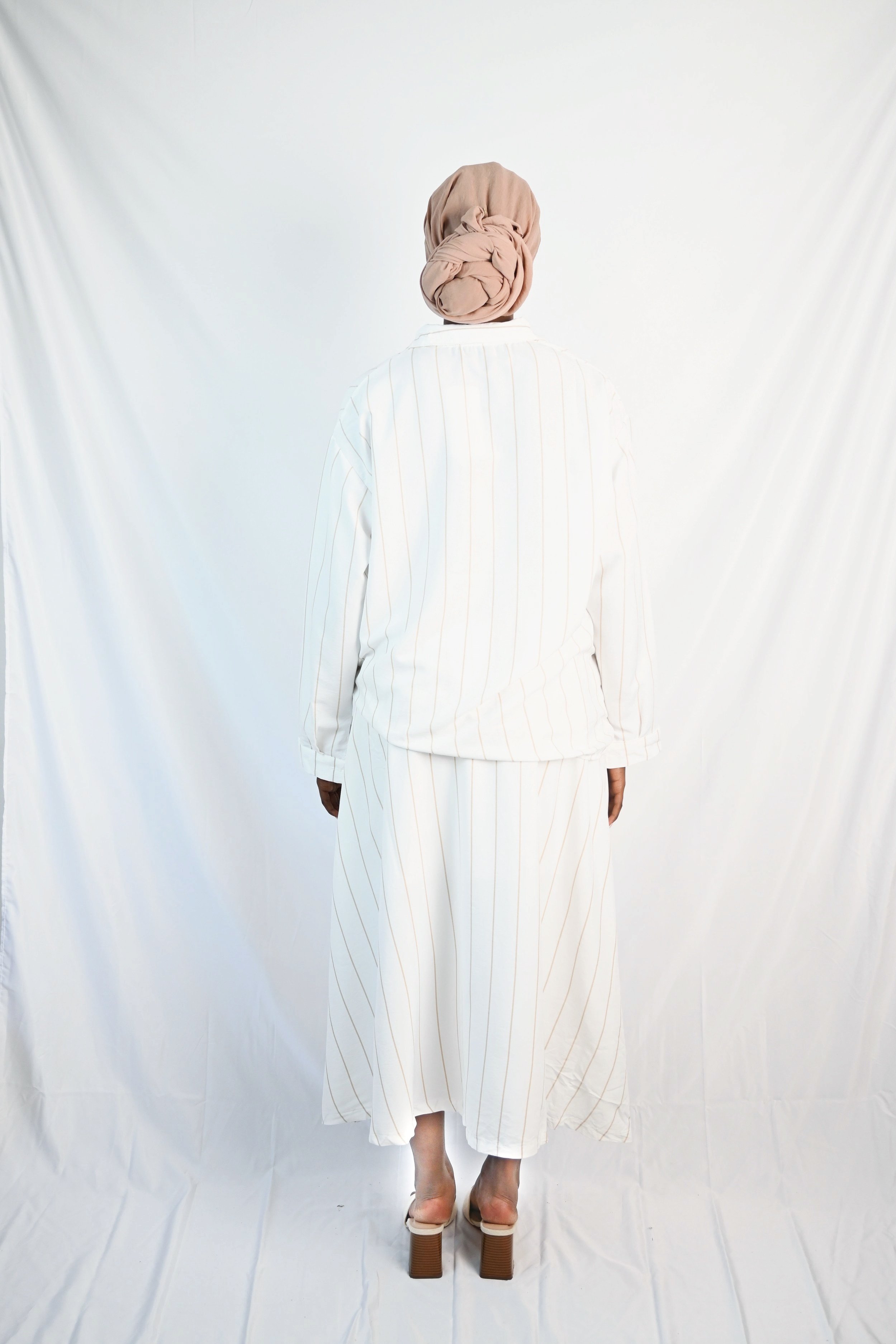 Frau trägt beige-gestreiftes Hemd mit passendem Rock, elegantes Set mit langen Ärmeln und fließendem Schnitt, perfekte Wahl für einen stilvollen, modernen Look.