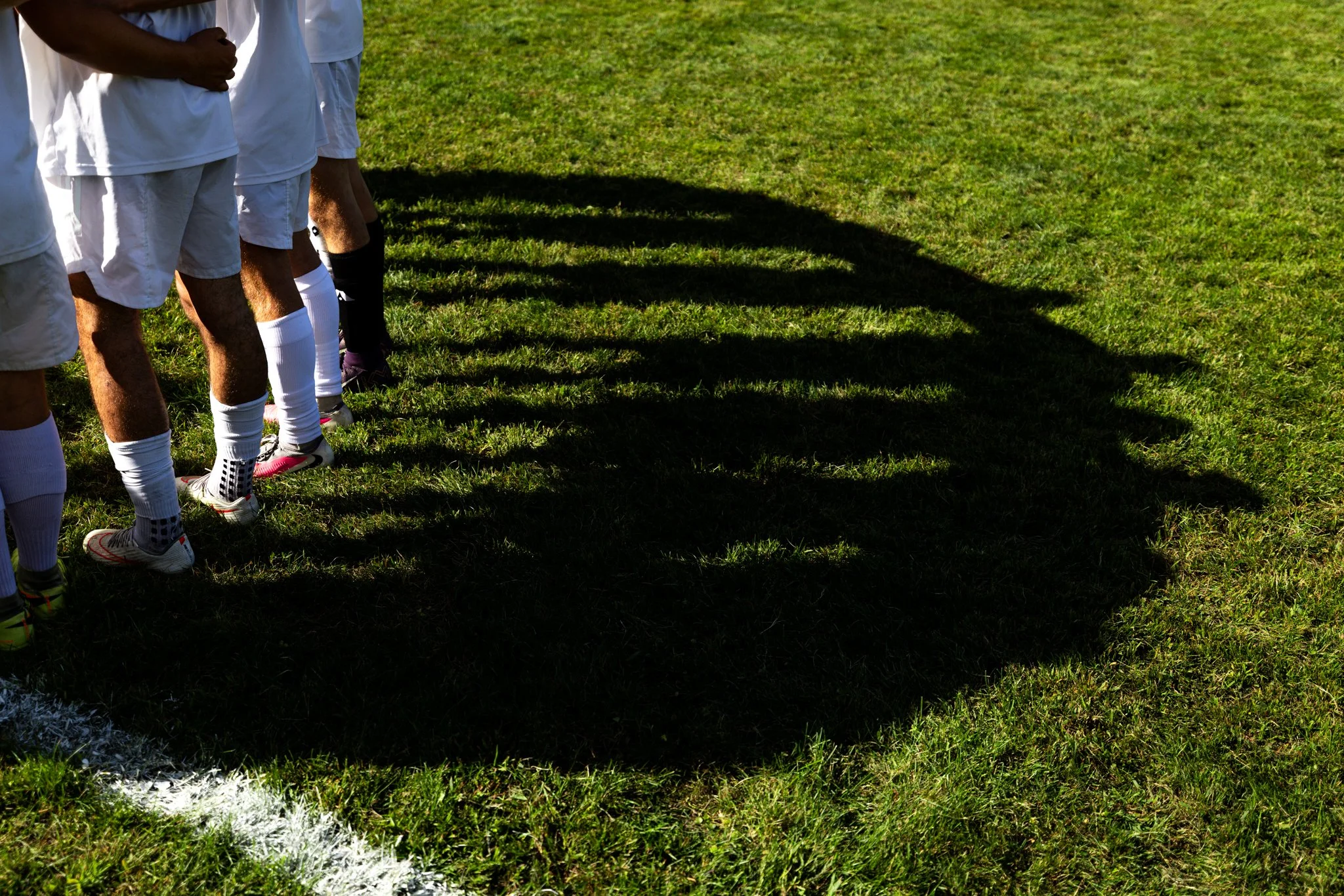 Player's shadows cast on the grass during a team huddle prior to Hampshire's boys varsity soccer game against Wahconah on Thursday, September 10th at Wahconah Regional High School in Dalton, MA.